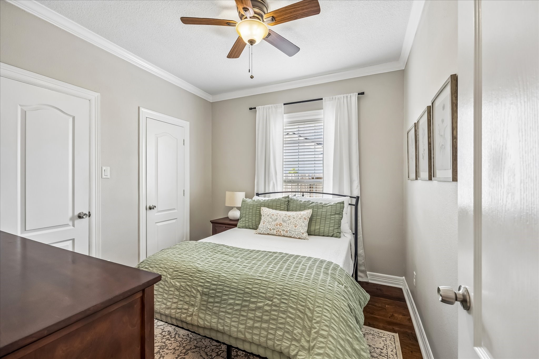 Secondary bedroom downstairs is finished with original hardwood floors refinished in 2020, crown molding, and windows on two sides.