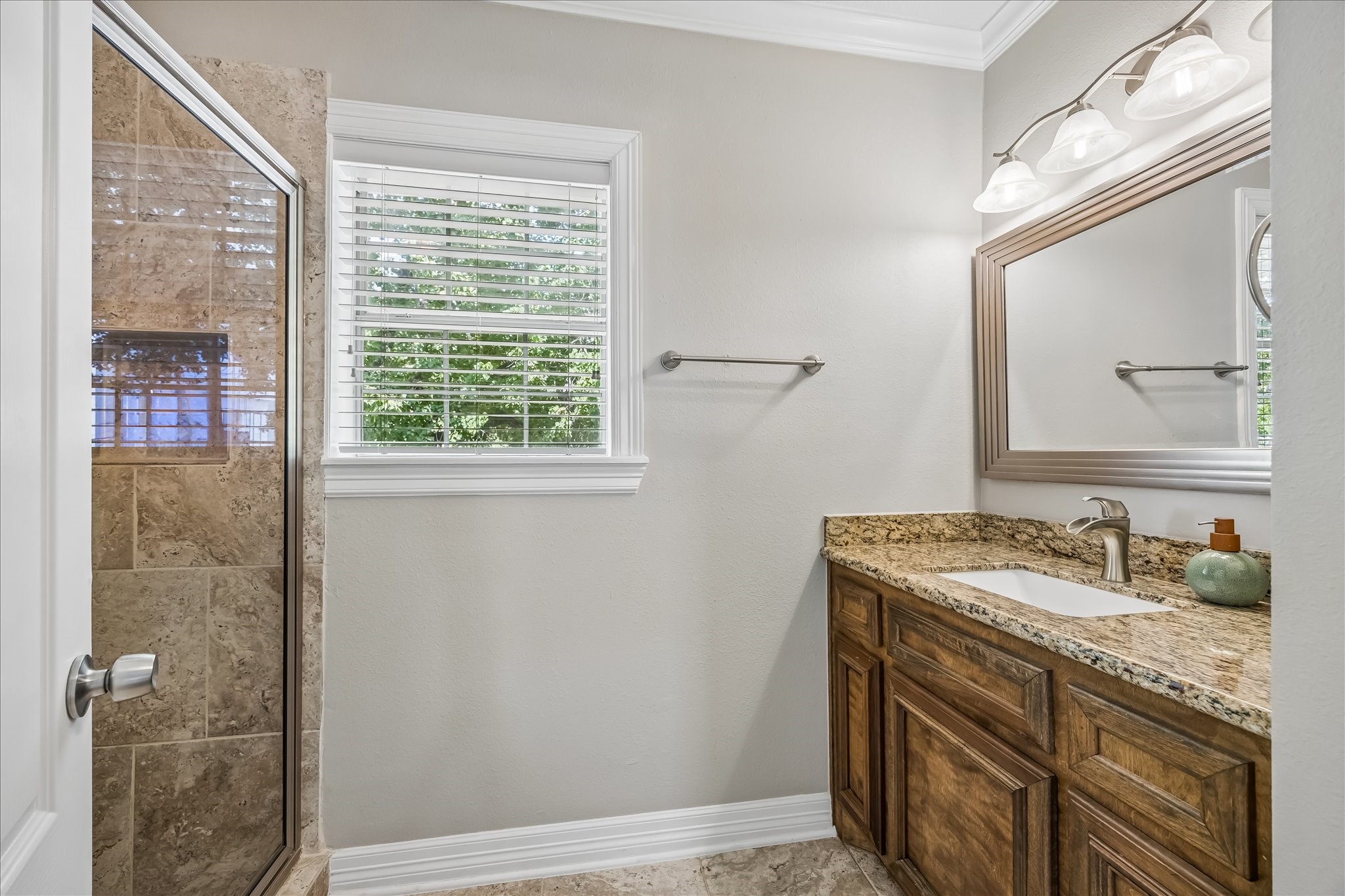 Secondary bath pairs a granite-topped wood vanity with a glass-enclosed stone shower and natural light from the window.