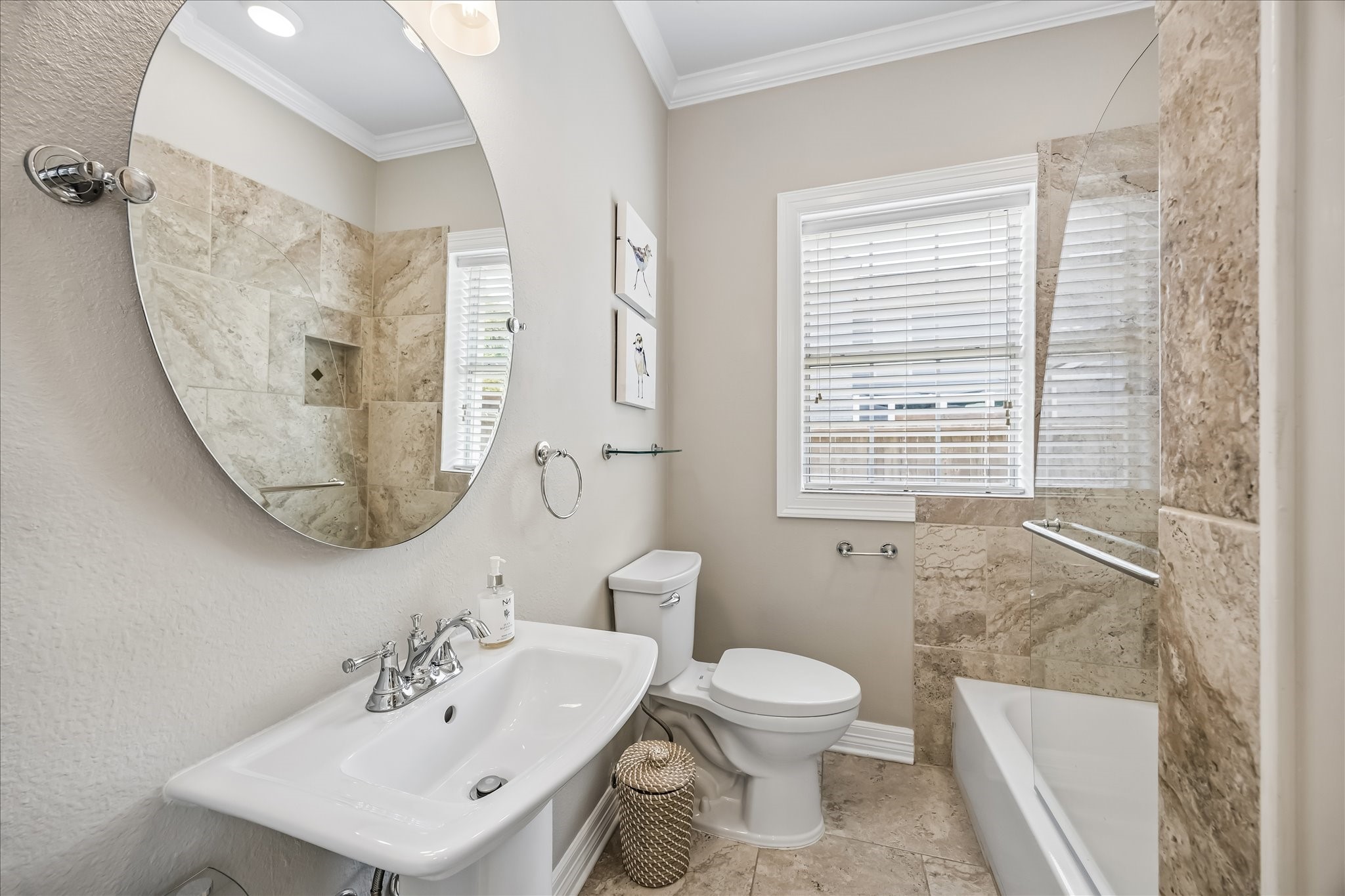 Full bath on the first floor offers a tub-shower combination, pedestal sink, large round mirror, and natural light.