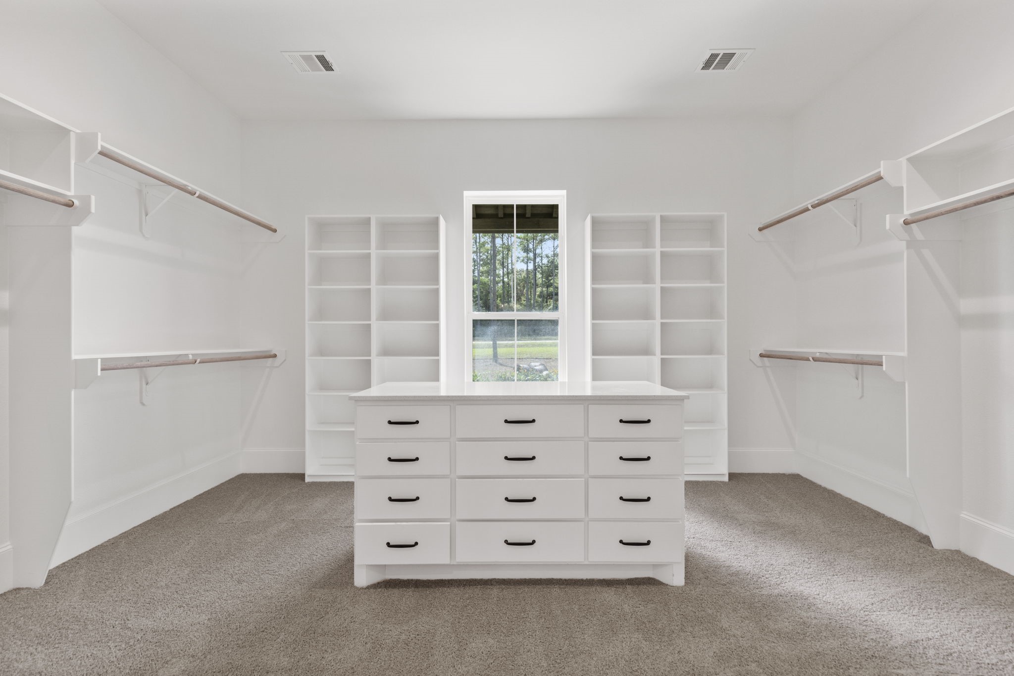 Spacious primary closet featuring custom shelving, generous hanging space, and a central packing island with extensive drawer storage.
