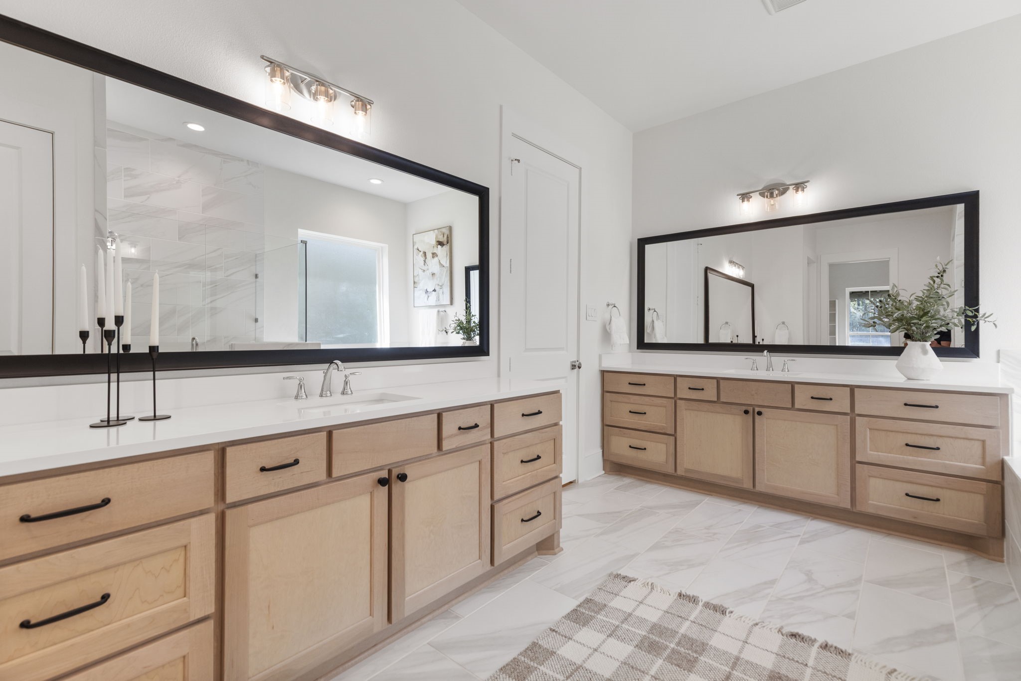 The primary ensuite features modern light wood dual vanities accented by matte black hardware and crisp white quartz countertops, contributing to a fresh, sophisticated aesthetic.