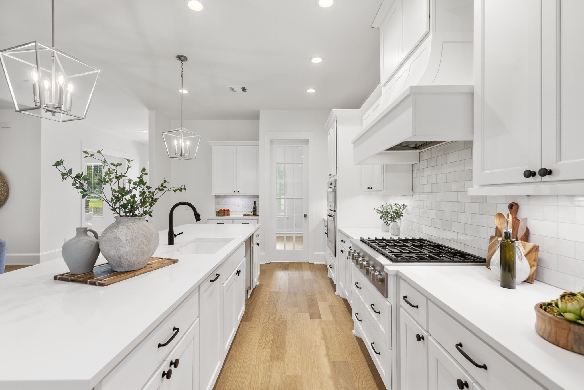 The matte black cabinet hardware provides a modern farmhouse aesthetic that perfectly complements the faucet, while the adjacent glass door opens into a spacious walk-in pantry.