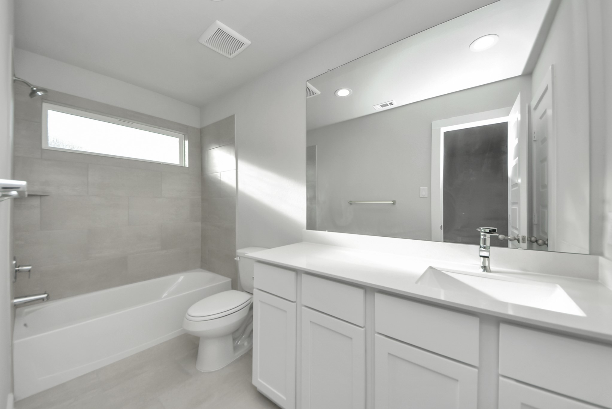 Secondary bath features tile flooring, bath/shower combo with tile surround, light stained wood cabinets, beautiful light countertop.