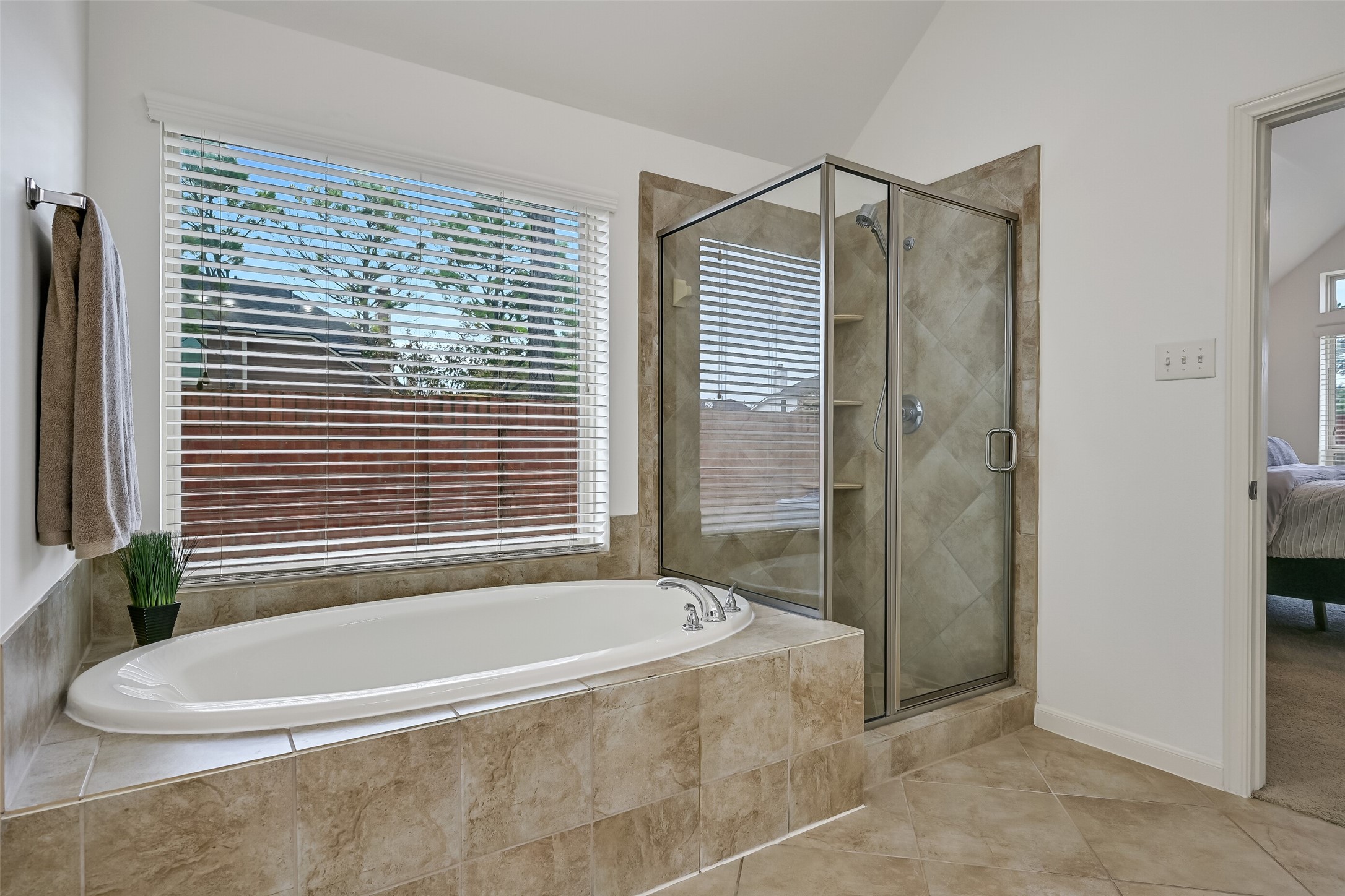 Unwind in the primary bathroom featuring a spacious soaking tub beneath a large window overlooking the backyard! A separate glass-enclosed shower with tiled surround & built-in corner shelves offers added convenience. Coordinating tile finishes, natural light & a spacious layout complete this relaxing retreat.