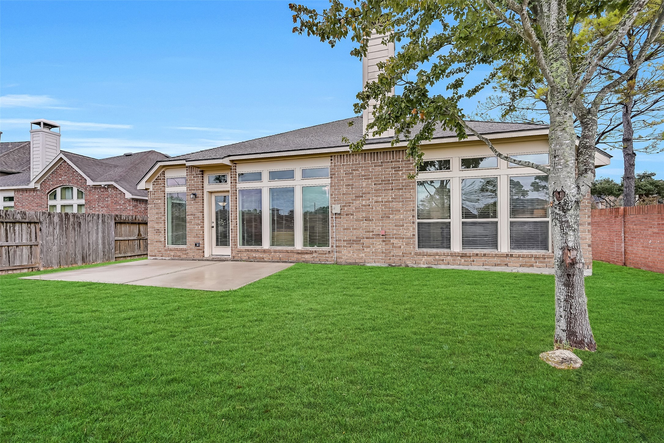 The home's attractive brick exterior continues around to the backyard, where an expansive concrete patio provides space for outdoor seating, grilling or dining. Tall windows with transoms above overlook the lush lawn, while a mature shade tree & substantial brick rear fence enhance the outdoor setting.