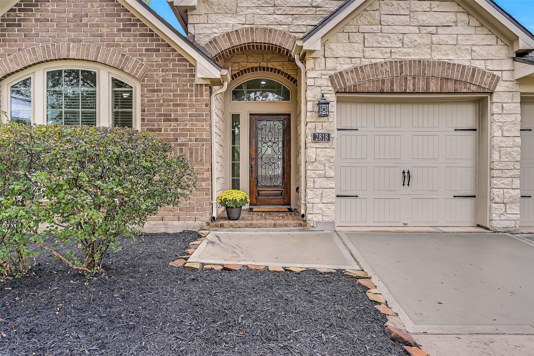 A closer look at the home's charming curb appeal reveals arched brick accents, textured stonework & an elegant wood-framed front door with decorative wrought-iron glass. An arched transom & sidelights welcome natural light into the entry, while fresh landscaping completes the inviting approach.