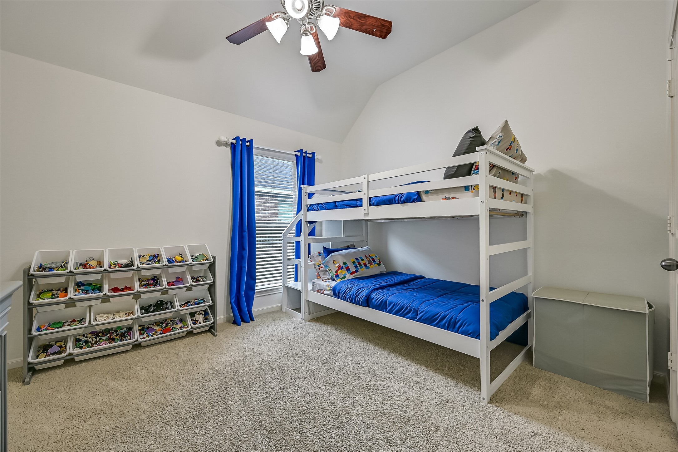 This inviting secondary bedroom features a vaulted ceiling, neutral carpeting, fresh light-colored paint & a ceiling fan. A large window with blinds welcomes natural light, while the generous walk-in closet provides excellent storage. One of three comfortable secondary bedrooms in this thoughtfully designed home.