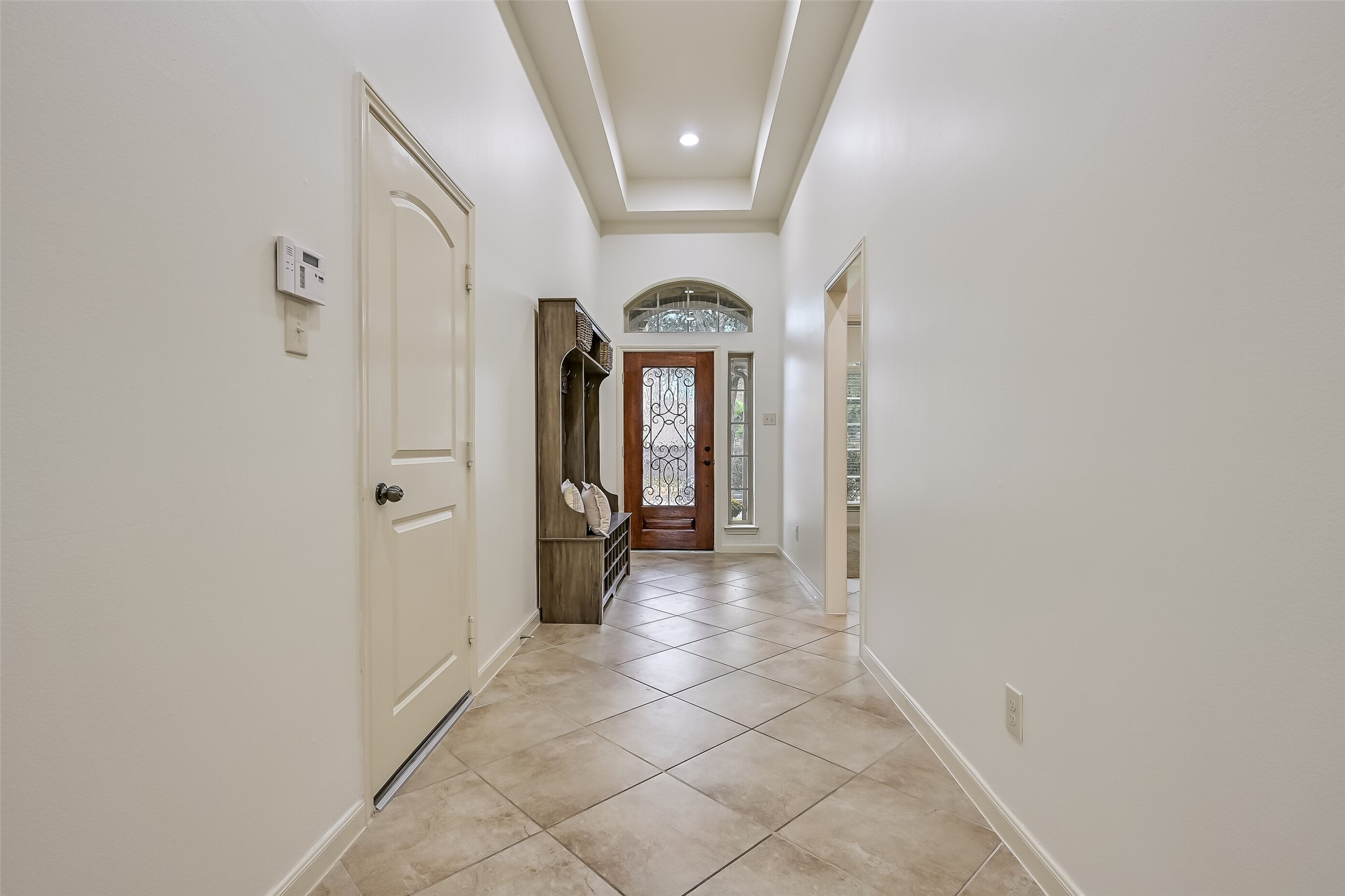 Looking back toward the front entrance, the extended foyer showcases a beautiful wood-framed door with decorative ironwork, glass sidelights & an arched transom window. The recessed ceiling with lighting, neutral tile flooring & crisp white trim complement the home's attractive architectural details.