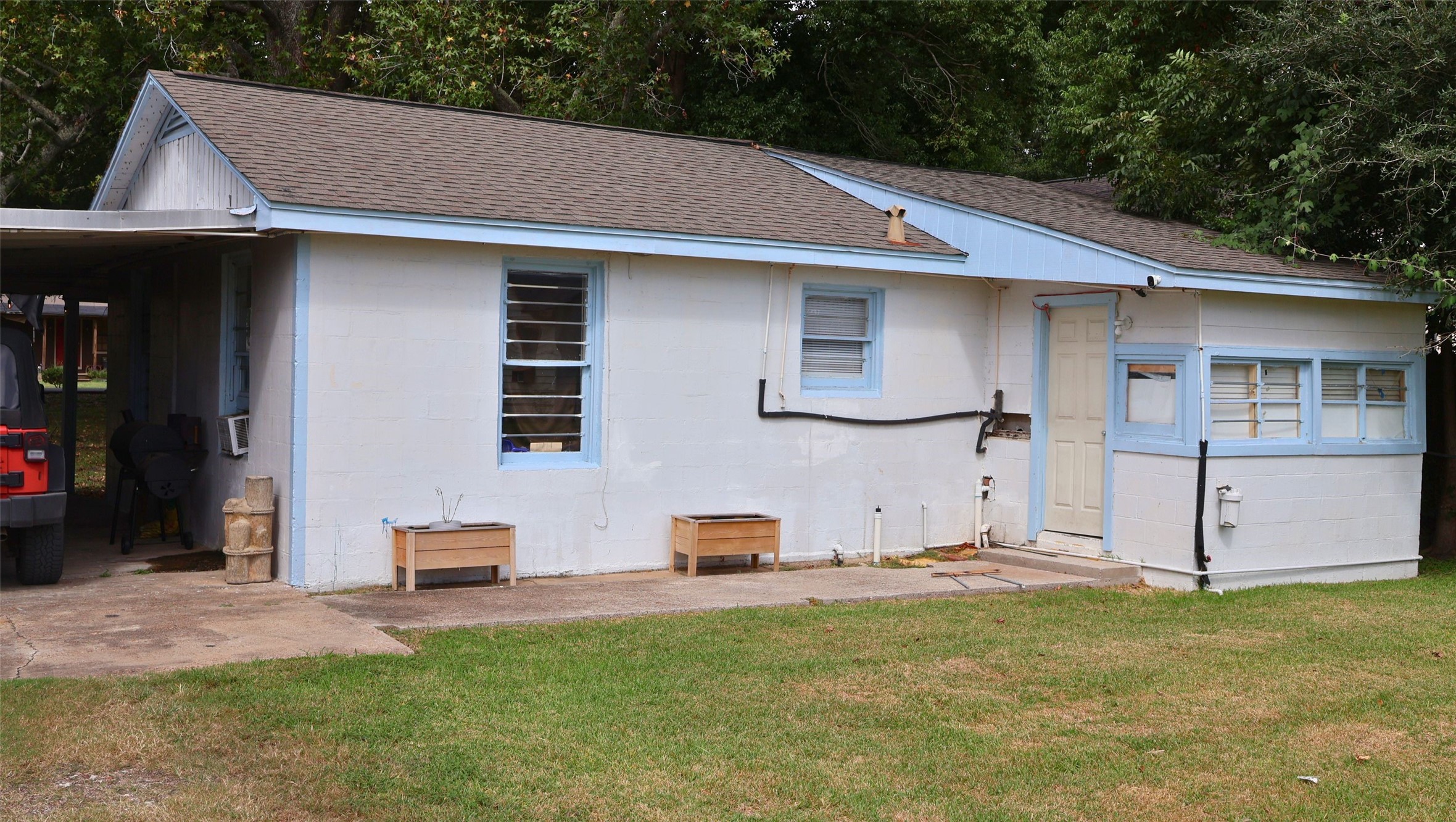 Cozy single-story home with charming blue trim and a convenient attached carport, nestled in a green, tree-lined yard.