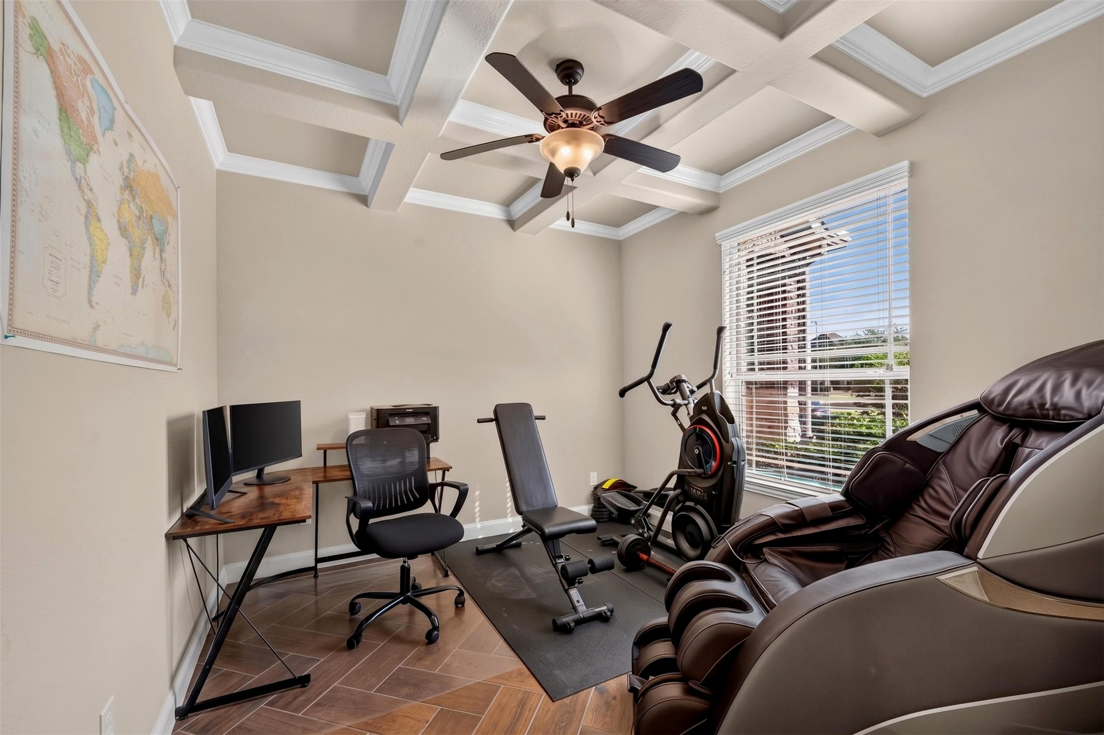 A versatile room provides space for a home office, workout equipment, or a combination of both. The coffered ceiling with crown molding adds architectural interest, while a large window brings in natural light.