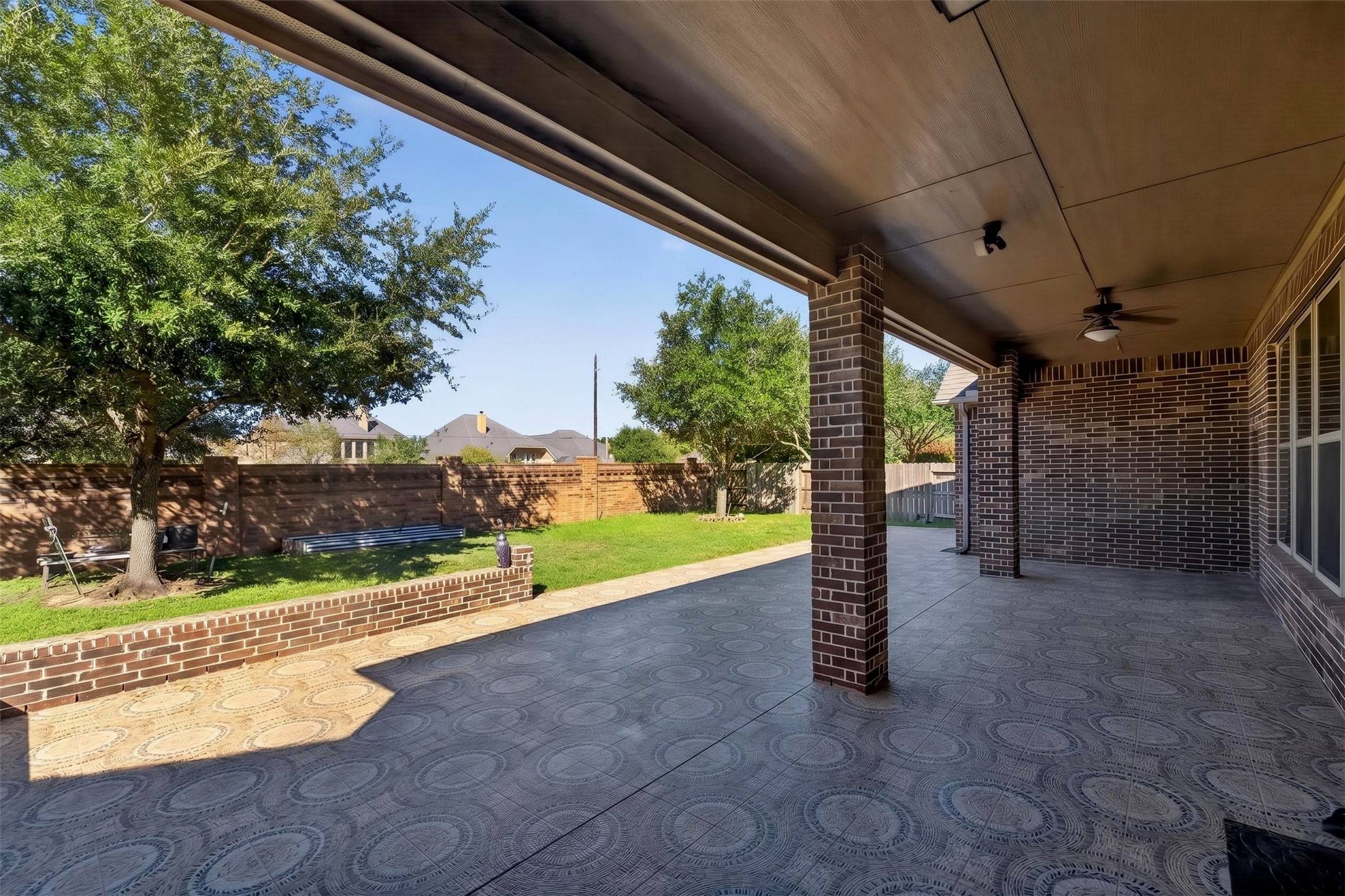 Extend your living space outdoors beneath the expansive covered patio, complete with a ceiling fan and ample room for seating or dining. The patterned patio flooring adds visual interest, creating an inviting setting for weekend gatherings or quiet evenings outside.