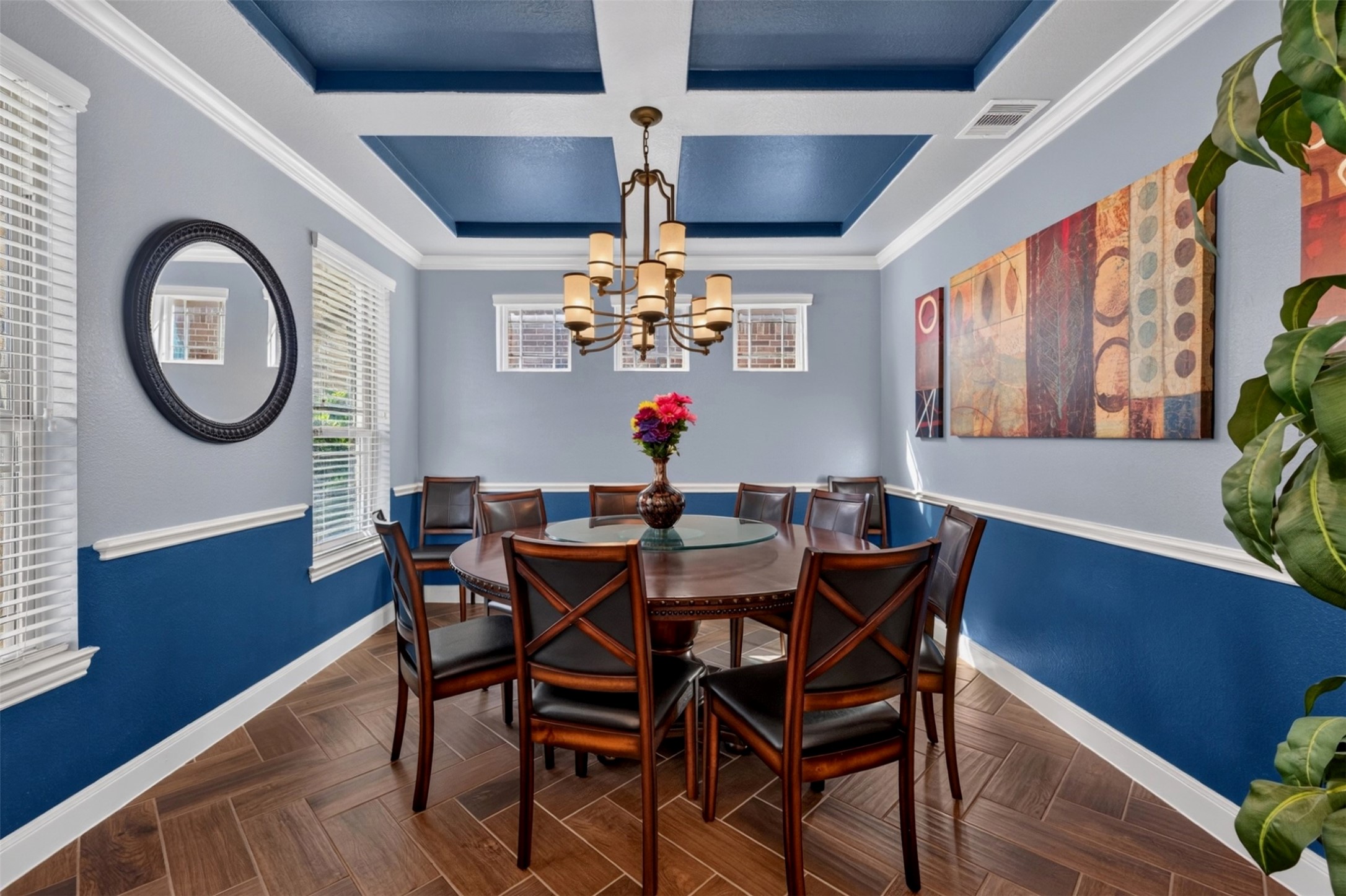 The ormal dining room, to the left of the entry, is designed to make gatherings feel special. The dramatic tray ceiling with contrasting blue inset, elegant chandelier, crown molding, and herringbone-pattern wood-look tile create a distinctive setting for holiday dinners and celebrations.
