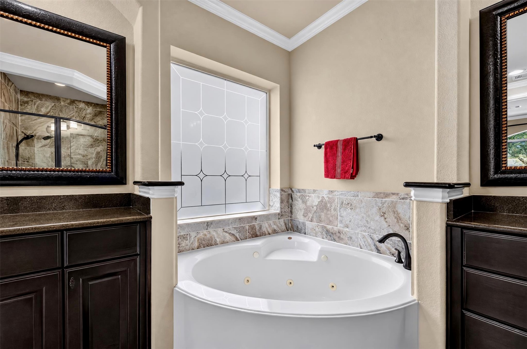 Enjoy a relaxing escape in the jetted soaking tub, framed by decorative tile accents and a distinctive geometric privacy window. The surrounding ledges and nearby cabinetry provide convenient places for bath essentials.
