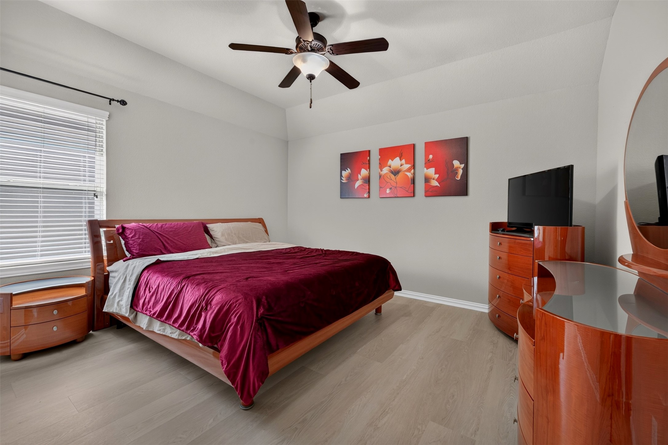 Warm wood furnishings complement the neutral finishes in this inviting bedroom. A ceiling fan, and a generous window reate a comfortable retreat for relaxing at the end of the day.