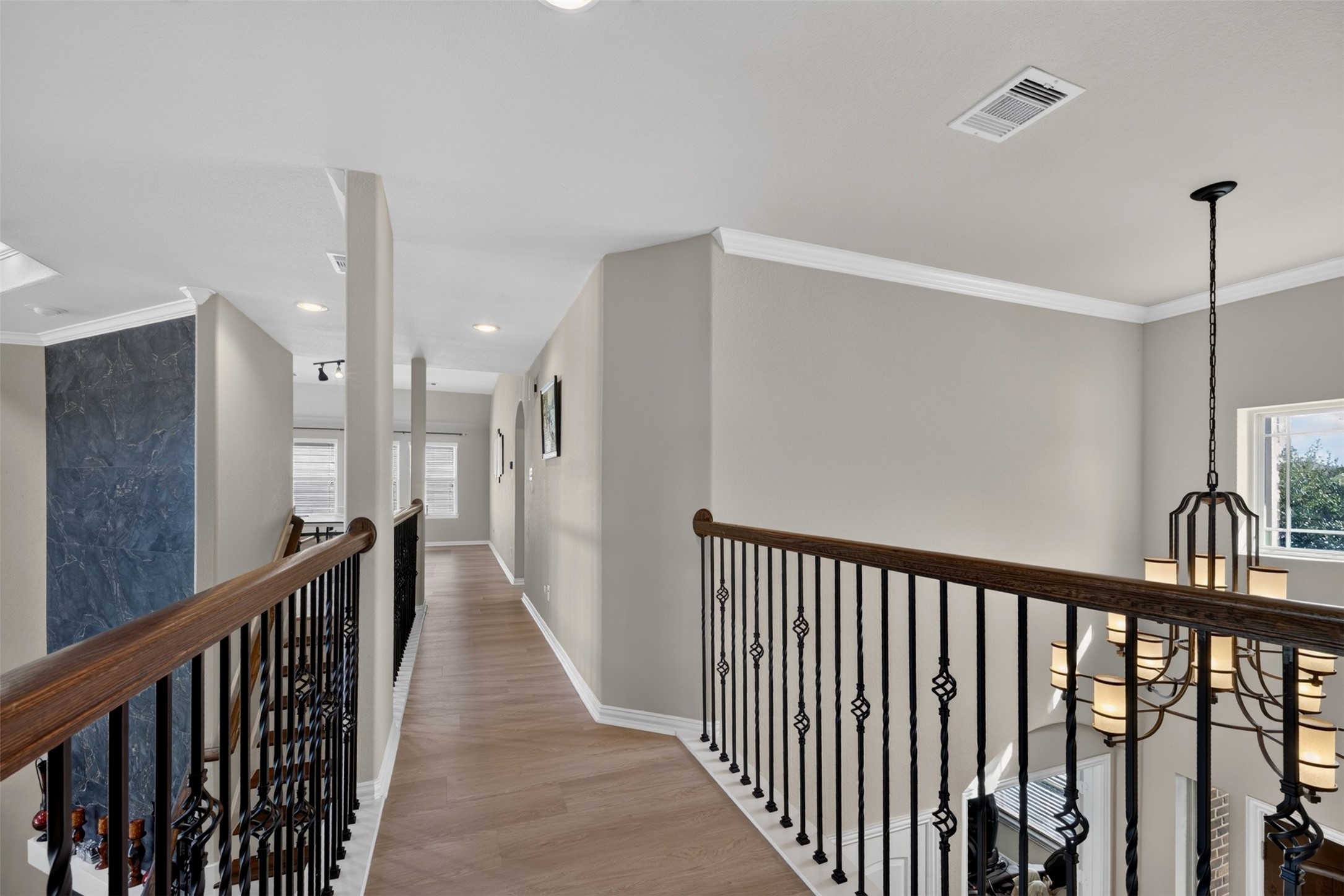 Wood-look flooring and decorative iron railing continue the home's architectural details along the hallway.