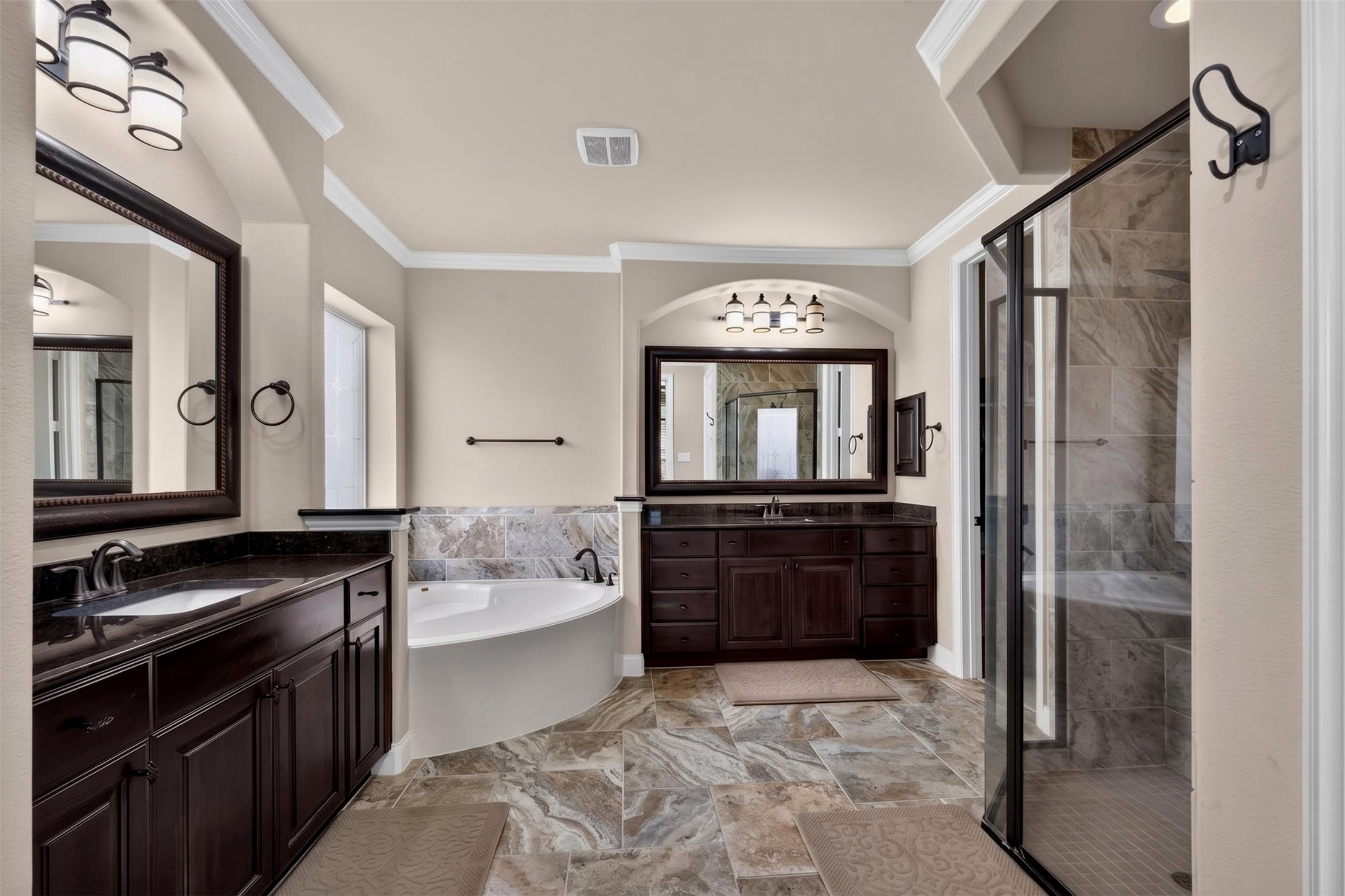 The primary bathroom welcomes you with rich espresso cabinetry, dark countertops, and framed mirrors that create a polished look. tThe spacious layout provides separate areas for daily routines.