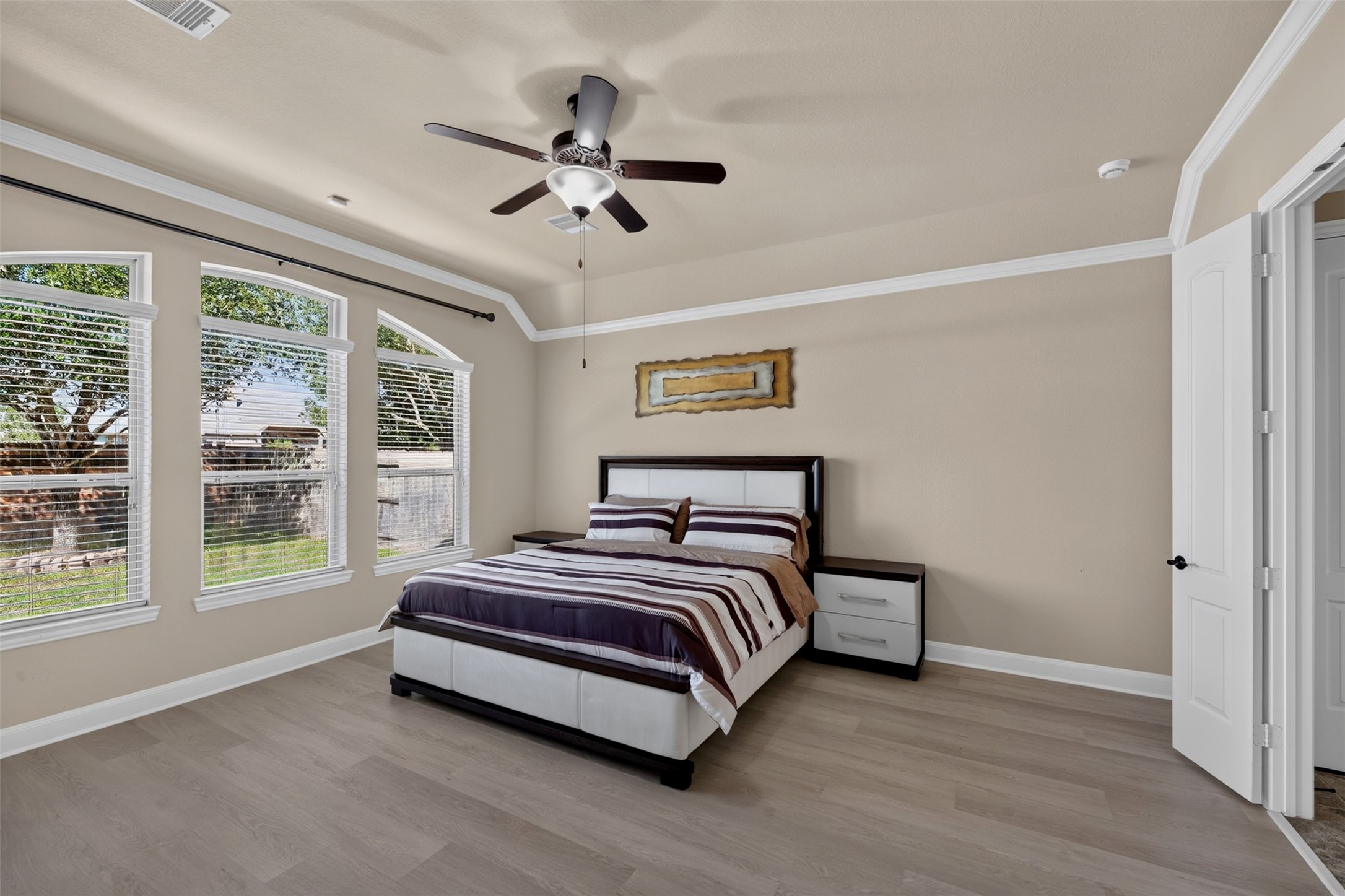 Step into the spacious primary bedroom, where soft neutral tones and an inviting layout create a comfortable retreat. Three large windows bring in natural light and offer views of the backyard, while the tray ceiling with crown molding adds an elegant finishing touch.
