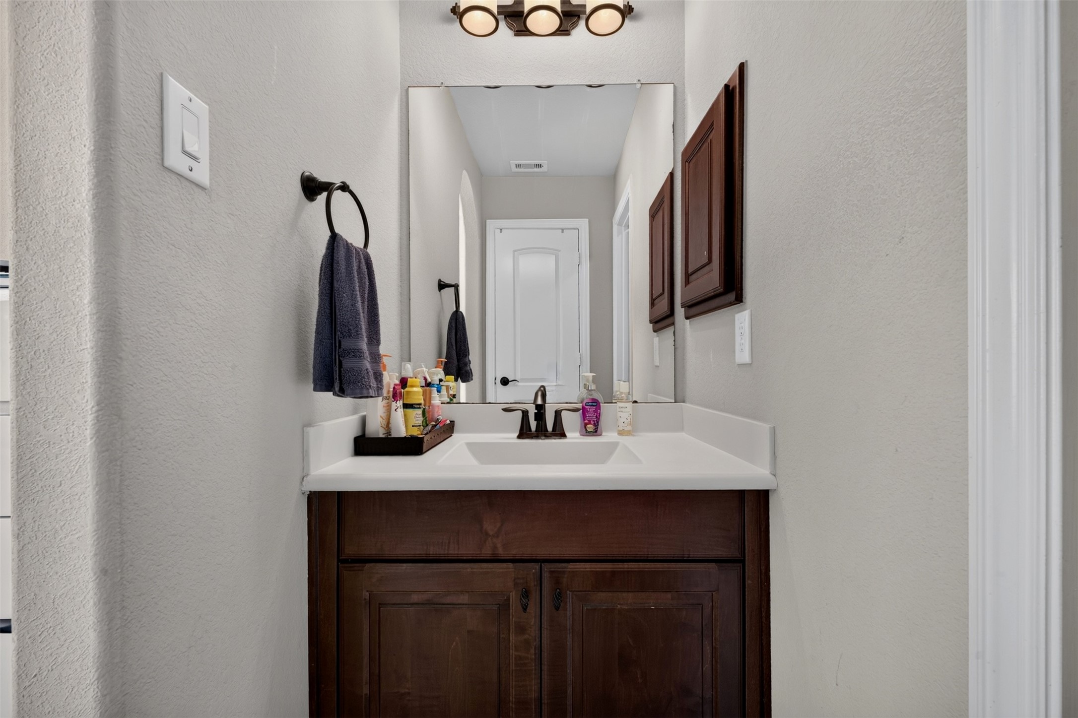 A generous vanity with a white countertop and rich wood cabinetry offers practical storage and everyday functionality. The large mirror and attractive light fixture complete this well-appointed bathroom space.