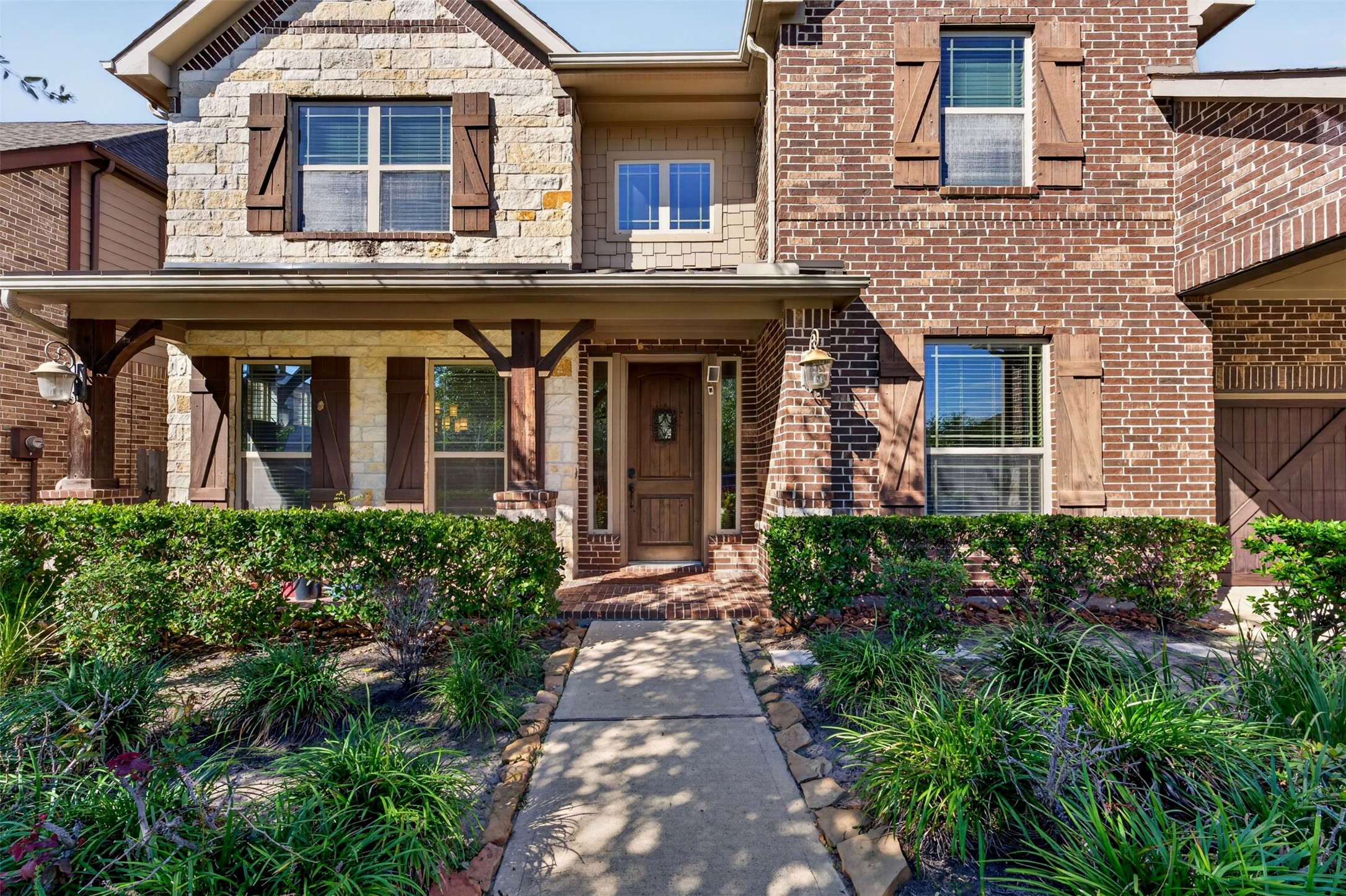 A closer look reveals the inviting front porch, wood entry door, and architectural blend of brick and stone. Thoughtfully arranged landscaping and shaded walkways add to the home's welcoming character.