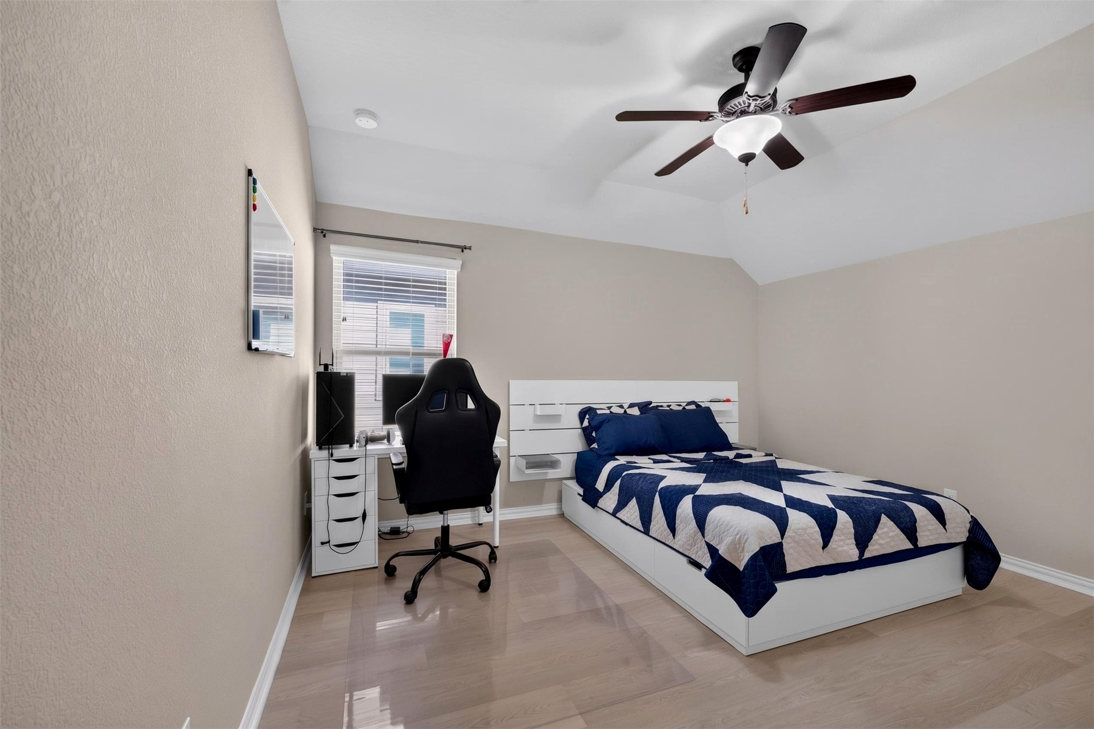 This upstairs bedroom features a vaulted ceiling that enhances the sense of openness, along with light wood-look flooring and a ceiling fan. Neutral finishes offer a flexible backdrop for a variety of furniture arrangements and personal styles. Opposite the bed is a double-door closet that provides convenient storage.