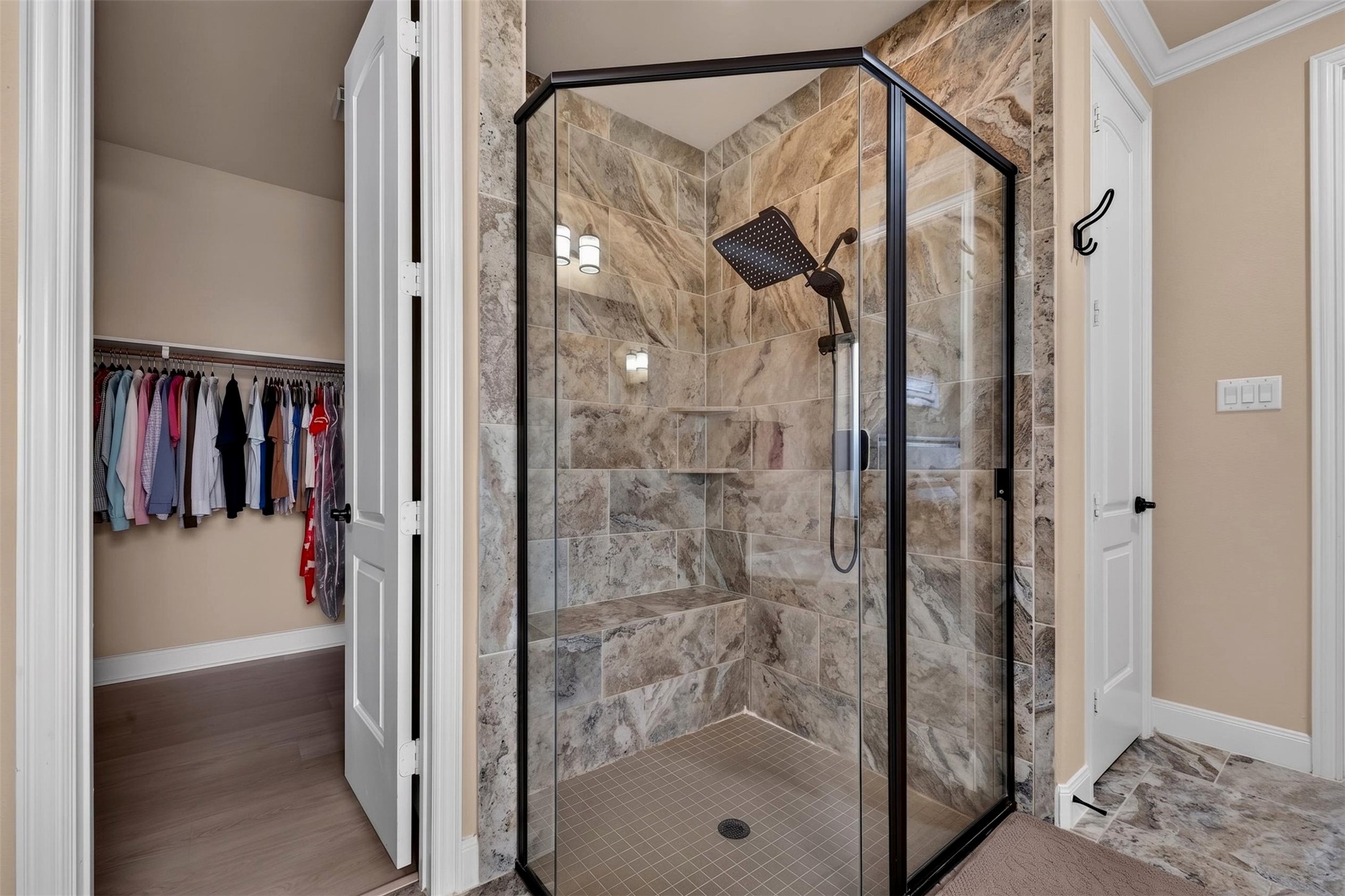 The oversized walk-in shower features floor-to-ceiling stone-look tile, a clear glass enclosure, and a built-in bench for added comfort. A rainfall-style showerhead and recessed niches bring both convenience and a spa-inspired feel to the design.
