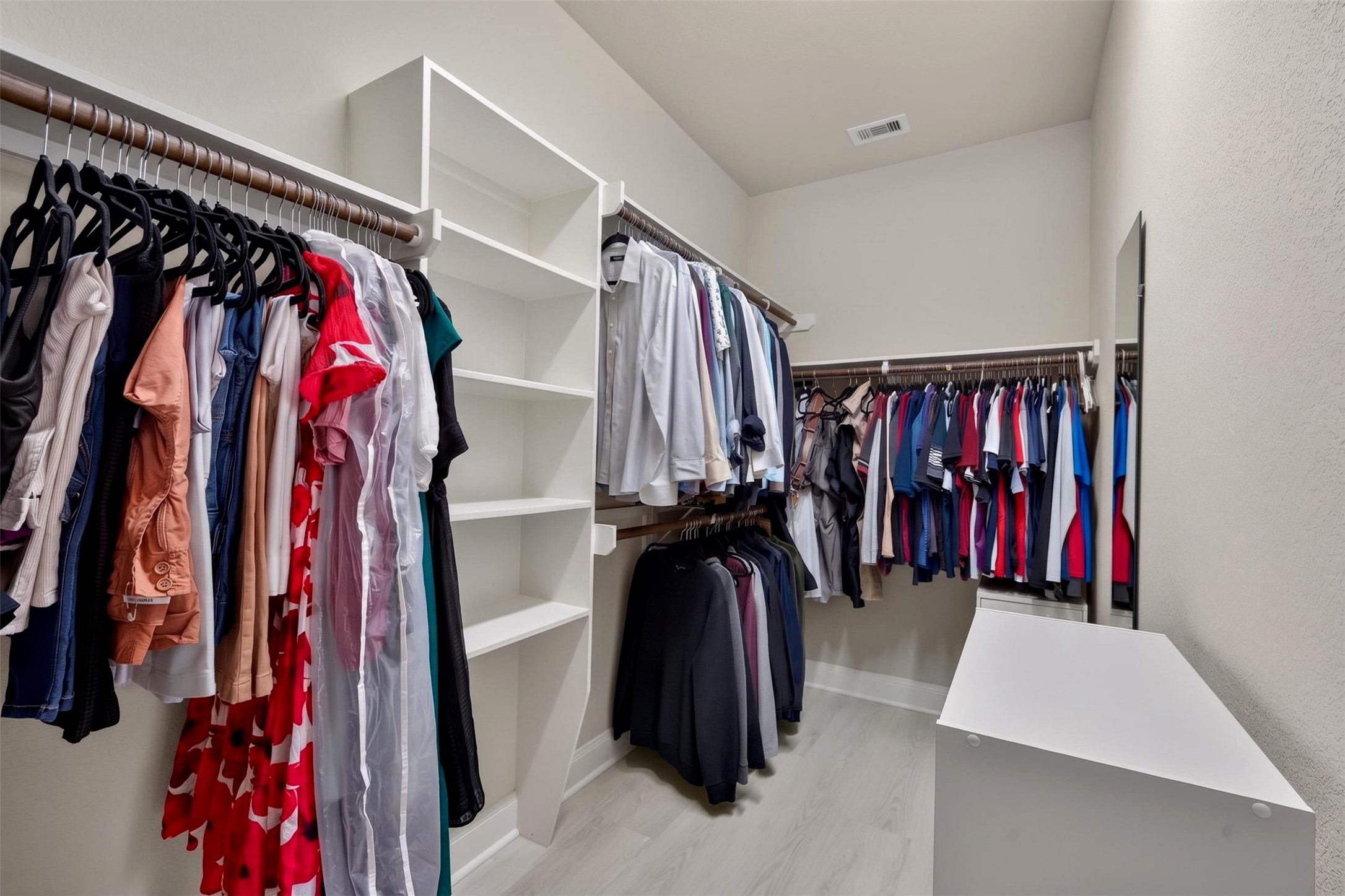 The walk-in closet offers extensive hanging space along multiple walls, complemented by open shelving for folded clothing and accessories. A central storage island adds another convenient spot to organize everyday essentials.