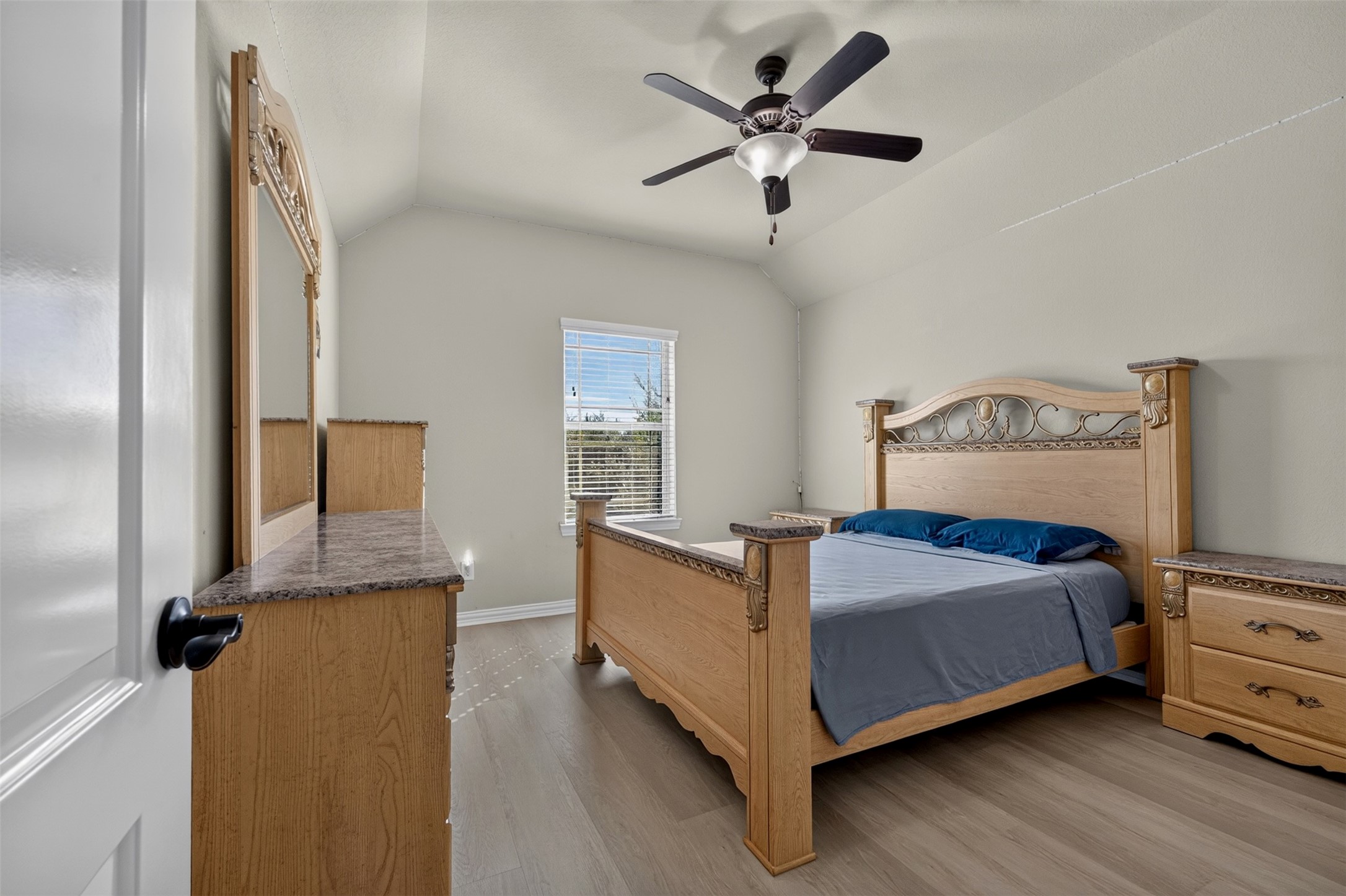 This bedroom offers a comfortable retreat with a vaulted ceiling, ceiling fan, and light-toned flooring. A window brings in daylight, while the spacious layout accommodates a full bedroom furniture arrangement.