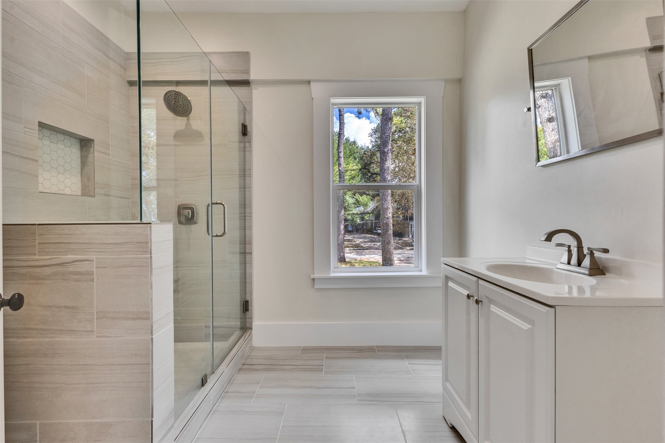 Modern bathroom featuring a spacious glass-enclosed shower, elegant tile work, and a bright window for natural light.