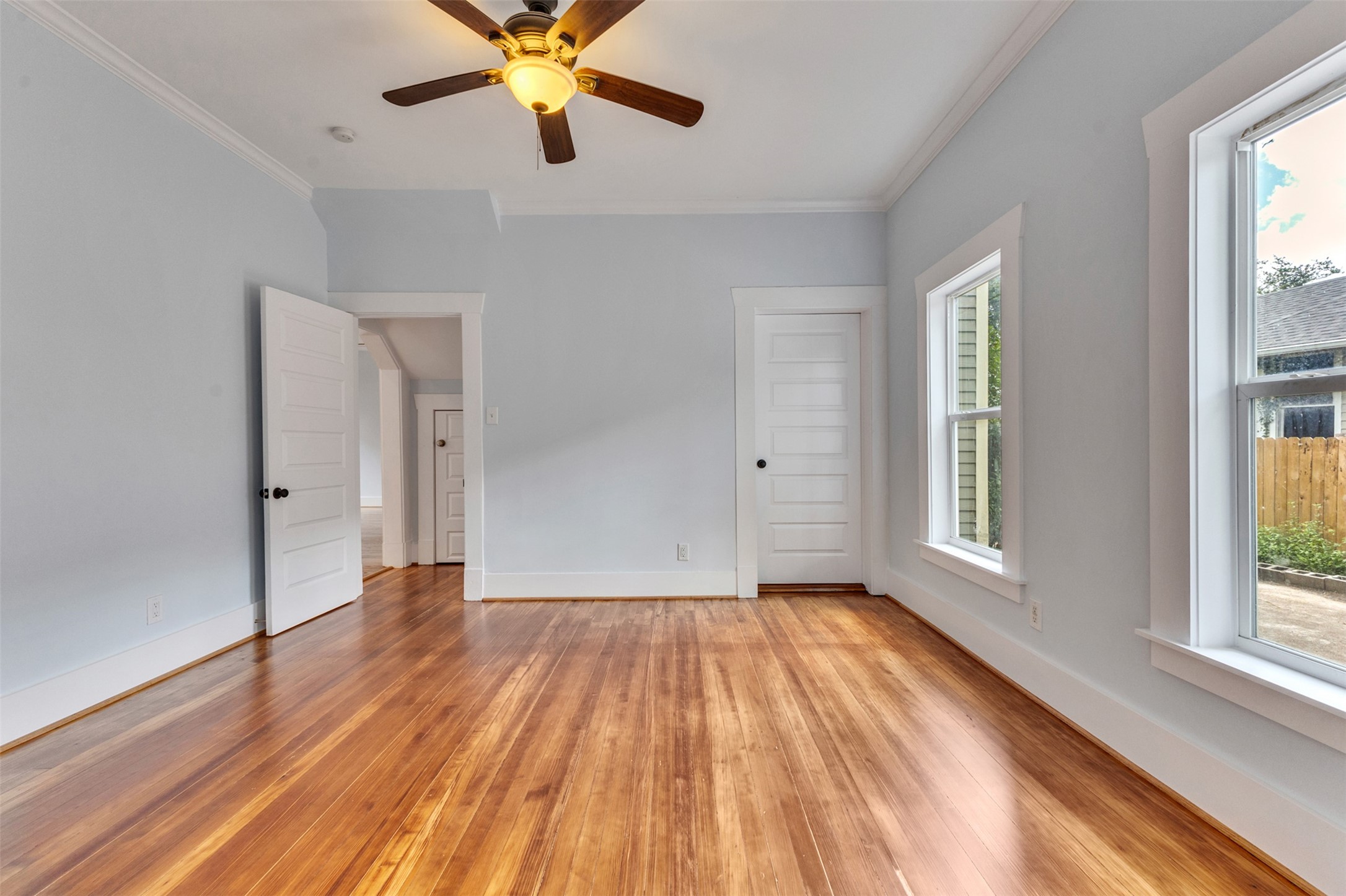 Bright and spacious room featuring rich hardwood floors, large windows for natural light, and a ceiling fan for comfort.