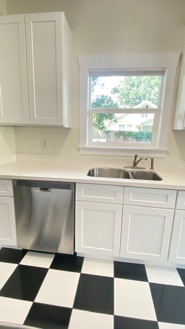 Bright kitchen featuring sleek white cabinets, a modern stainless steel dishwasher, and a charming black-and-white checkered floor.