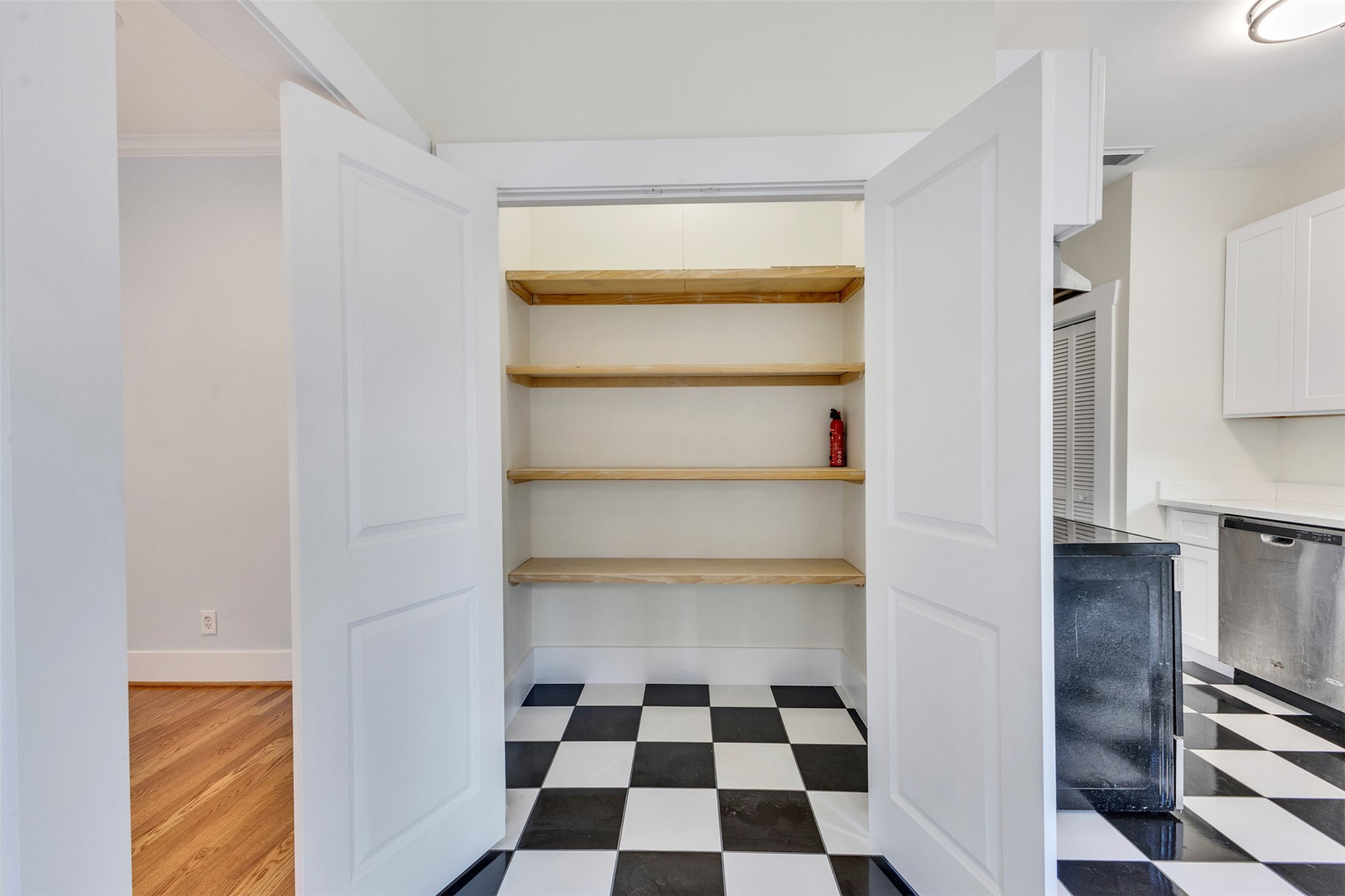 Spacious pantry with open shelving and classic black-and-white checkered flooring, blending seamlessly into a modern kitchen with stainless steel appliances.