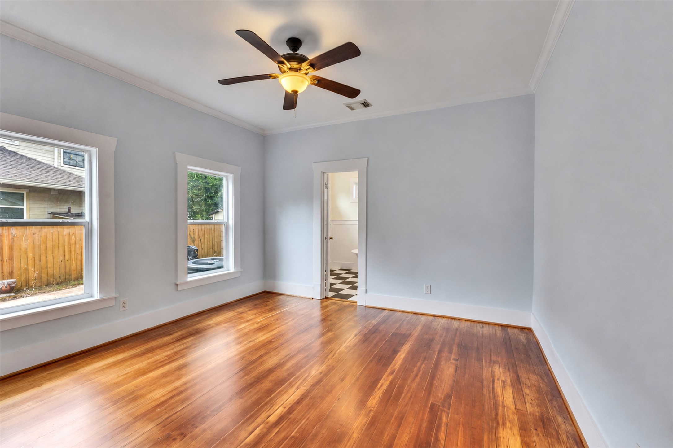 Spacious room with beautiful hardwood floors, abundant natural light from large windows, and a ceiling fan for comfort.