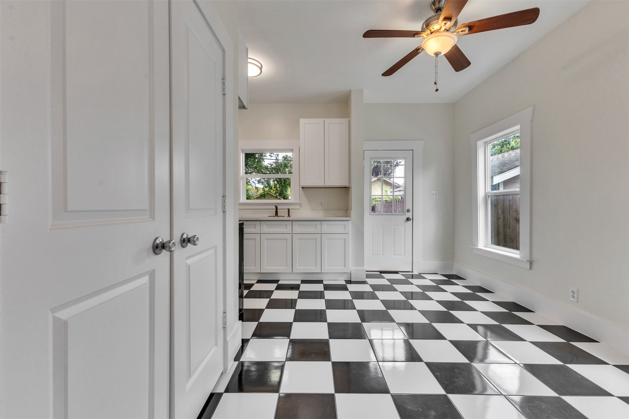 Bright kitchen with stylish black and white checkered flooring, modern ceiling fan, and ample natural light from large windows.