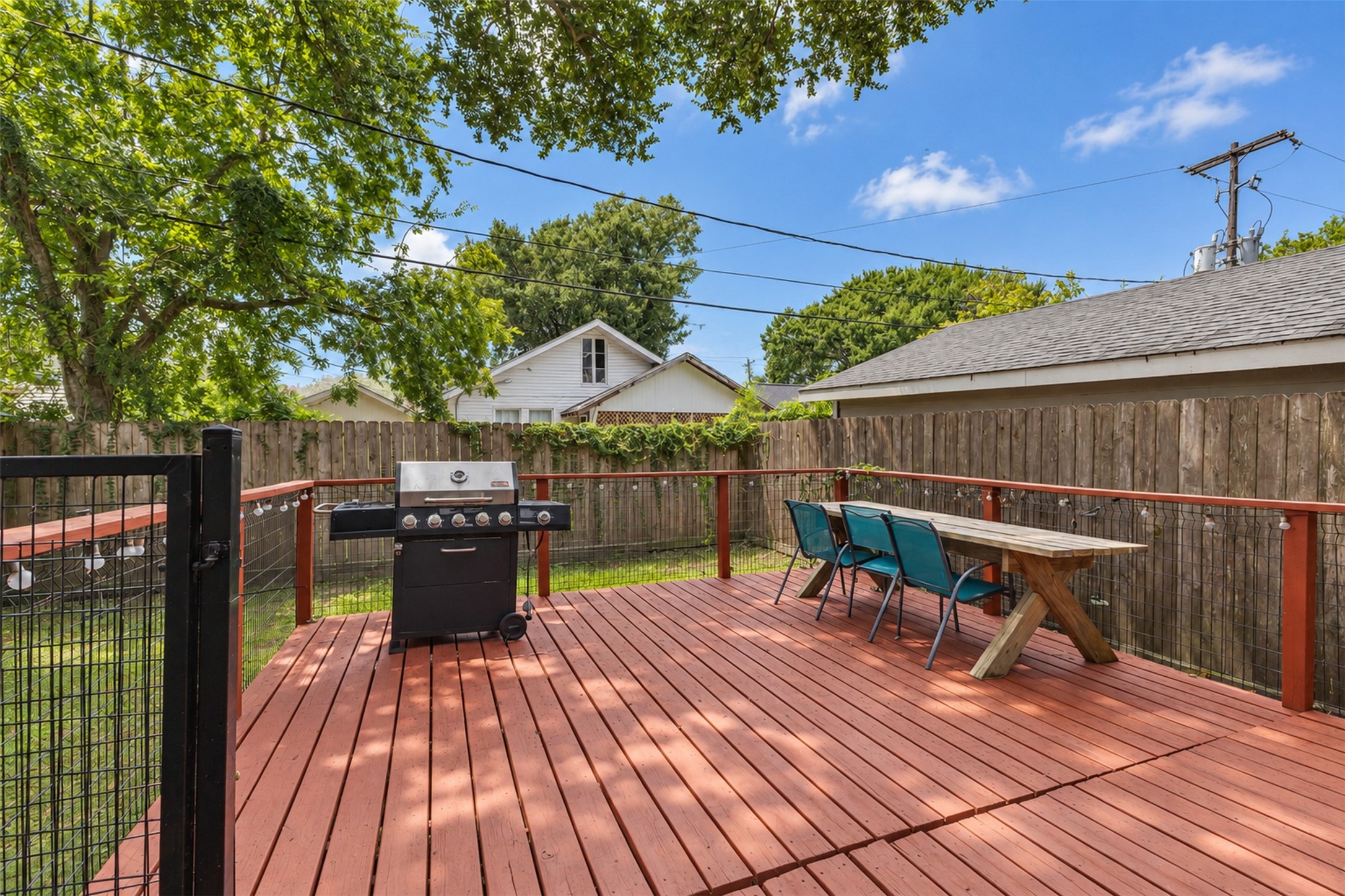 Spacious backyard deck perfect for entertaining, featuring a built-in grill and ample seating under the shade of mature trees.