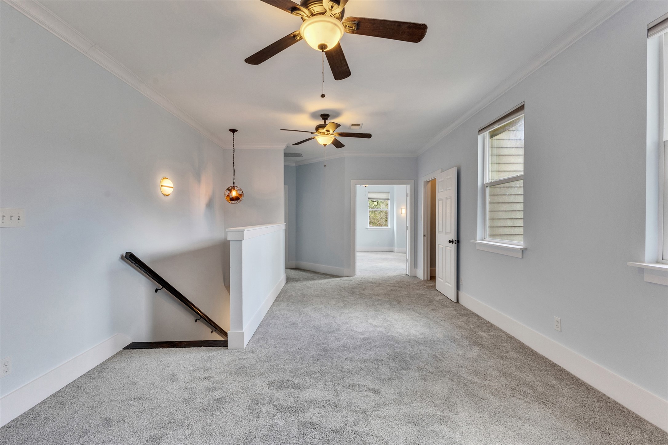 Spacious hallway with plush carpeting, ceiling fans, and ample natural light, leading to a bright room.