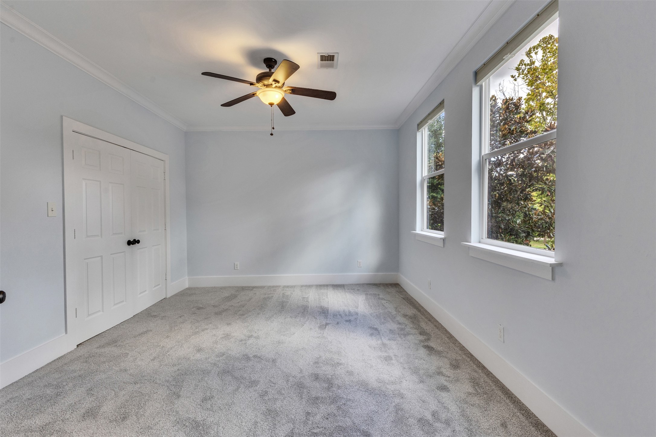 Bright and airy bedroom featuring soft carpet, a ceiling fan, and ample natural light from large windows, offering a serene and cozy space.