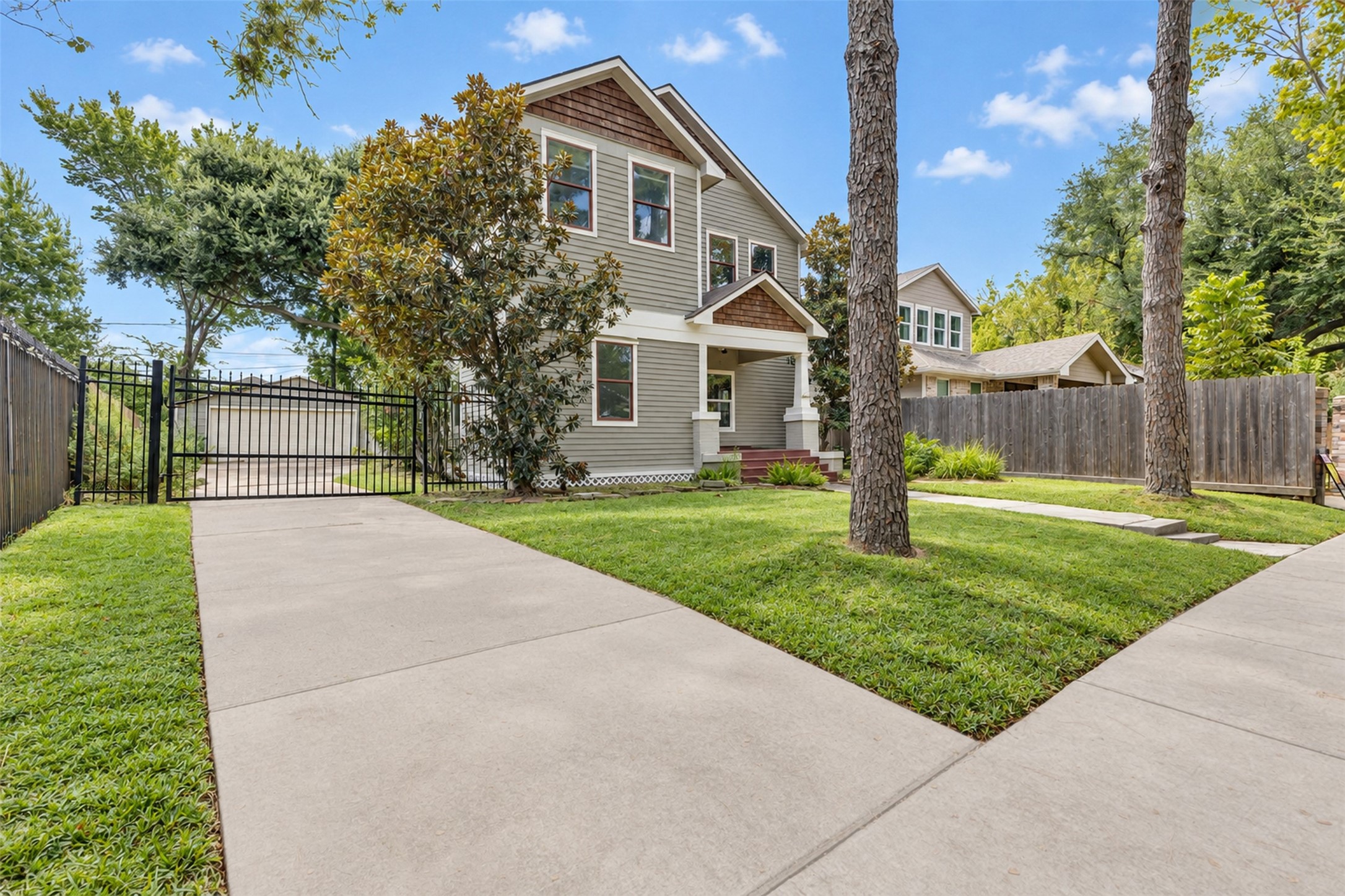 Charming two-story home with a welcoming front porch, nestled behind mature trees and featuring a gated driveway for added privacy.