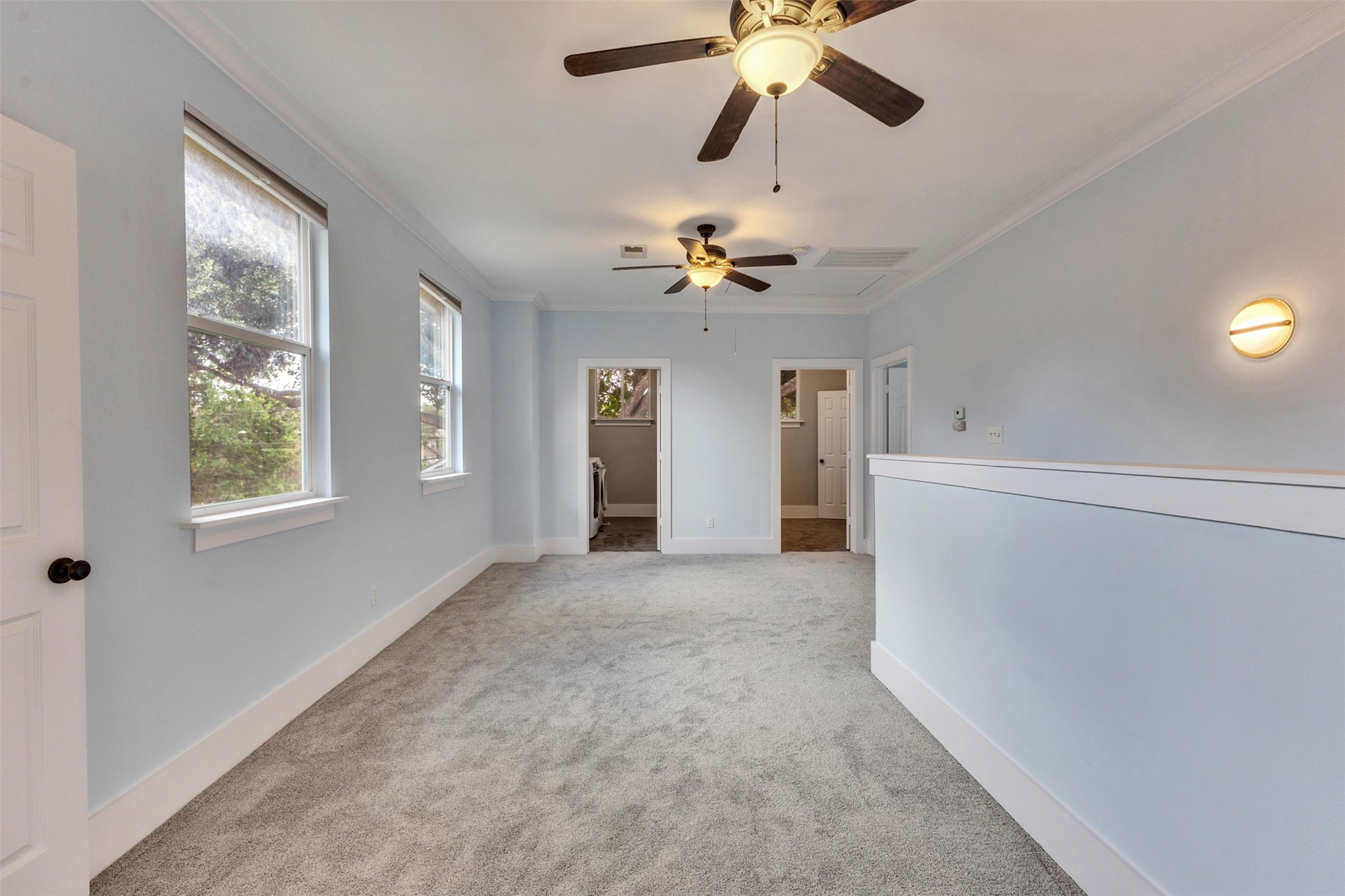 Spacious room with soft carpeting, neutral walls, and ample natural light from multiple windows, featuring ceiling fans for added comfort.