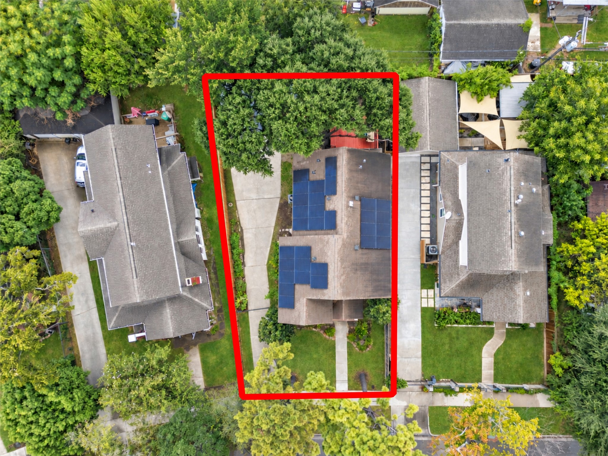 Charming home with solar panels, nestled between lush greenery, featuring a long driveway and ample backyard space.