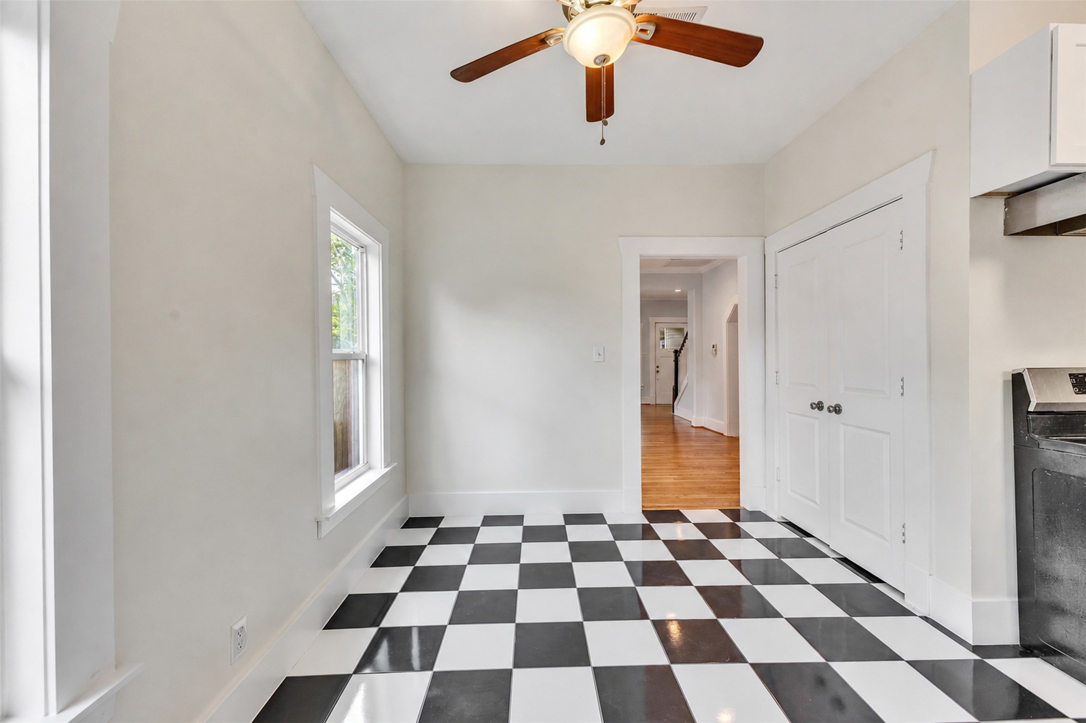 Bright and welcoming space featuring classic black-and-white checkered flooring, a ceiling fan, and ample natural light from a large window, perfect for a cozy dining area or breakfast nook.