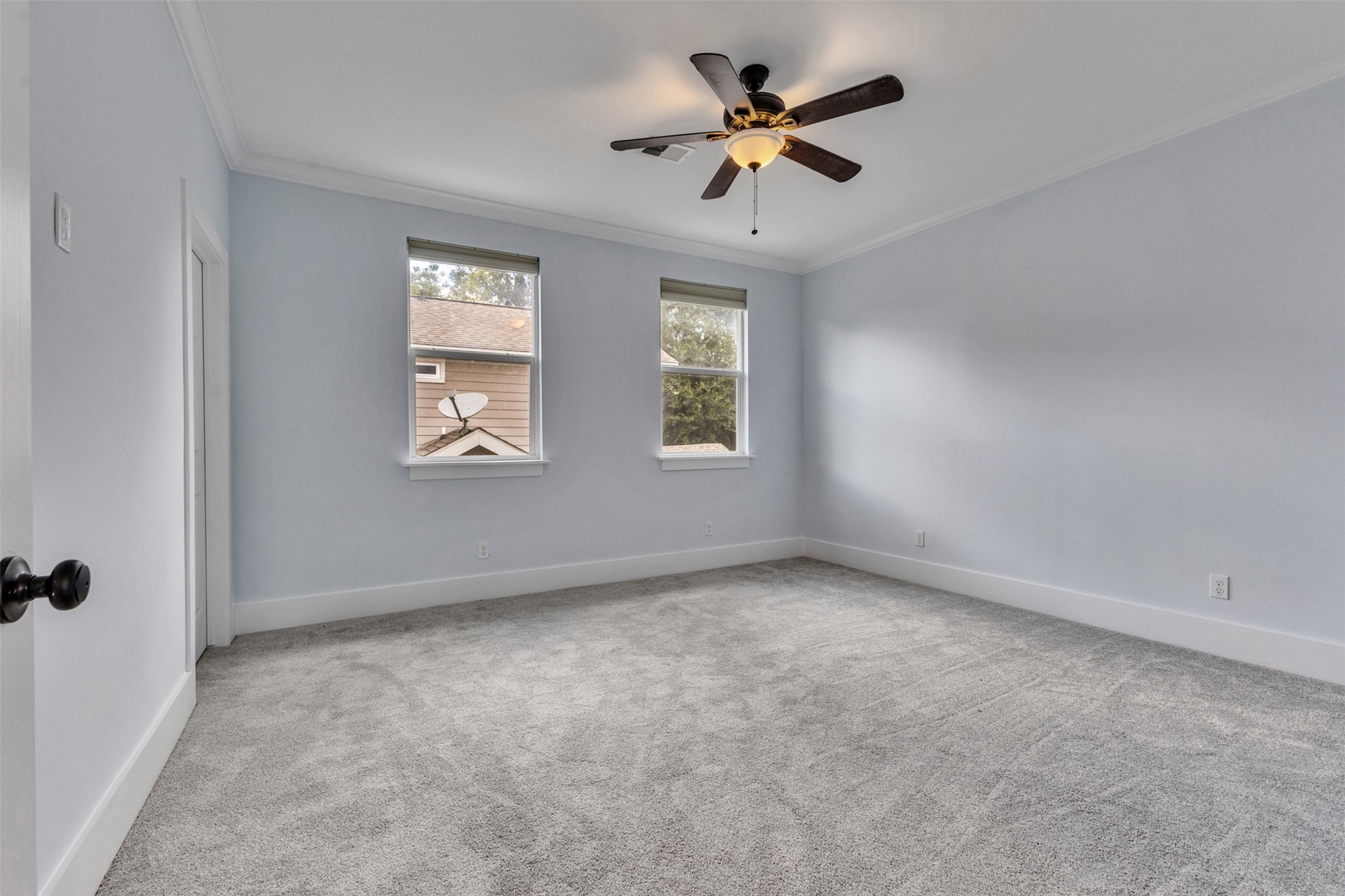 Spacious bedroom featuring soft gray carpeting and ample natural light from two large windows, complemented by a modern ceiling fan.