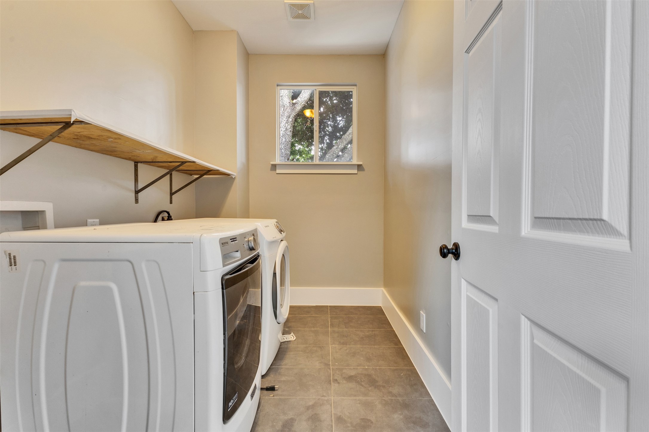 Modern laundry room with sleek appliances, ample storage, and natural light from a large window.