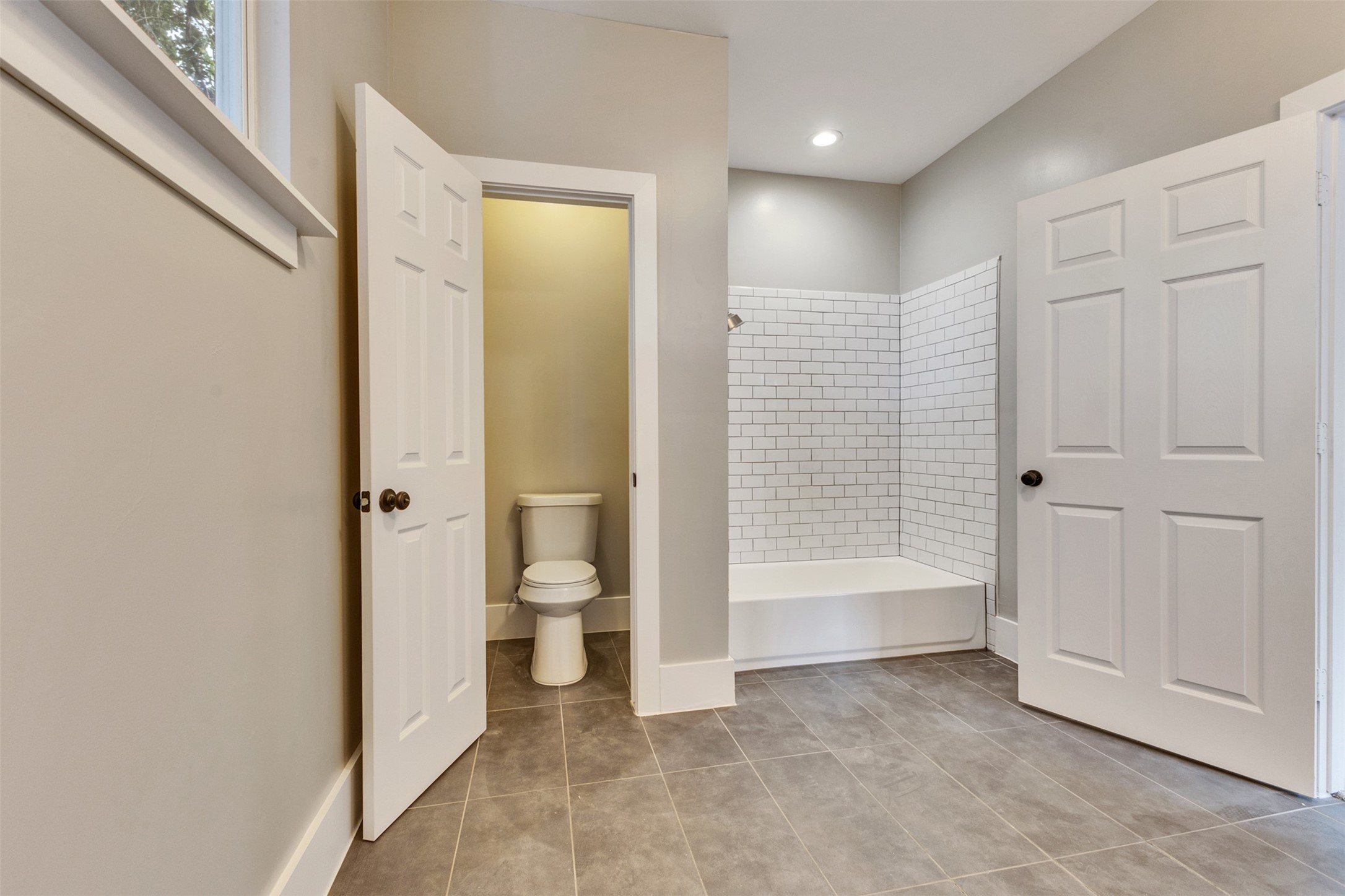 Spacious bathroom featuring sleek gray tile flooring, a classic subway-tiled shower, and a separate toilet area for added privacy.