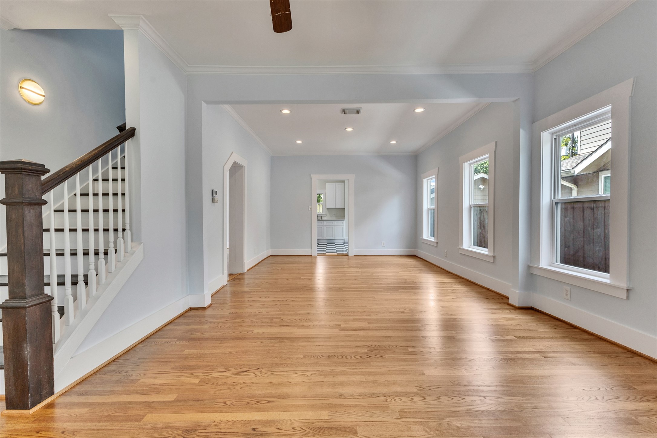 Spacious open-plan living area with beautiful hardwood floors, abundant natural light from multiple windows, and a classic staircase leading upstairs.