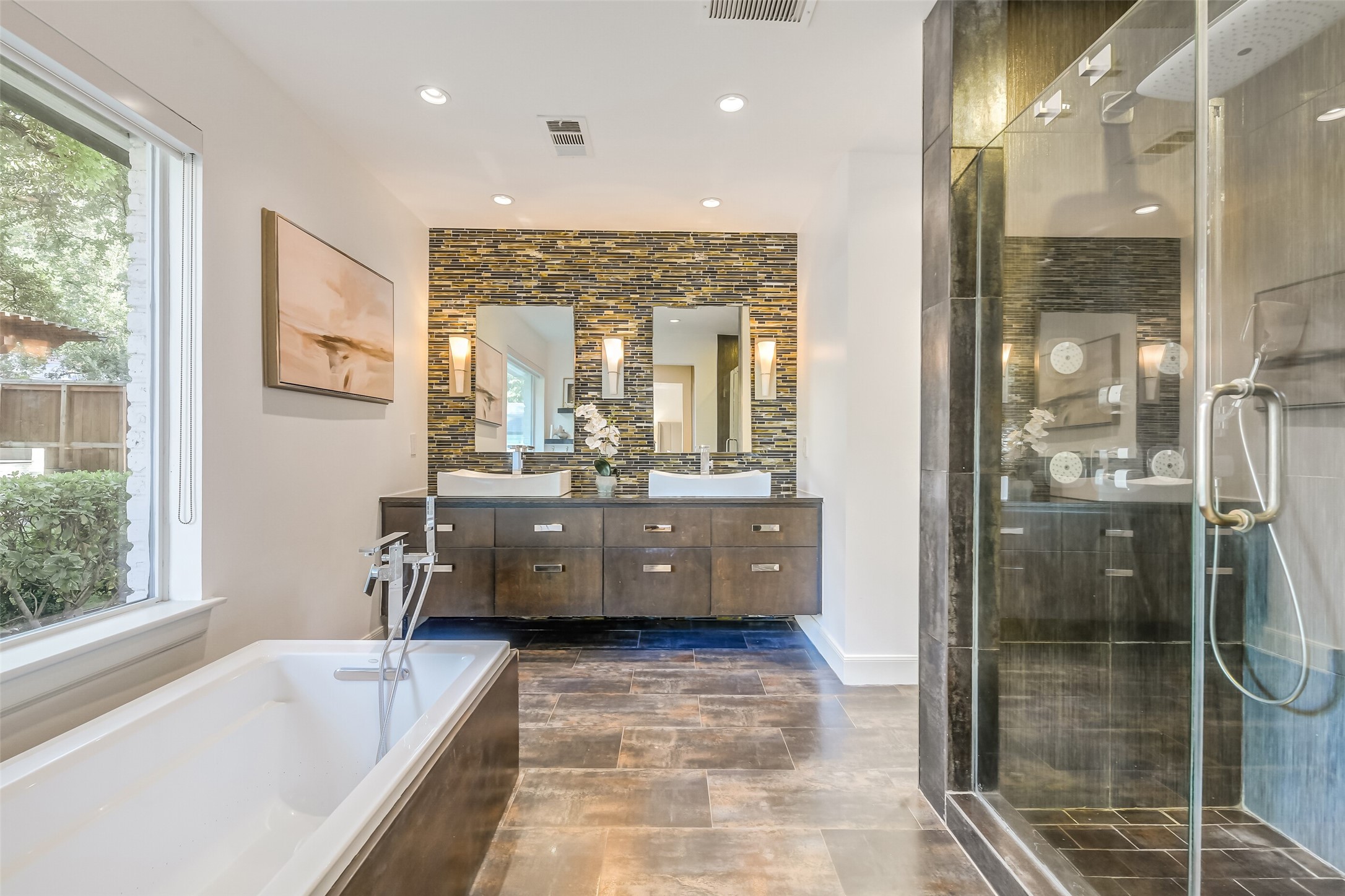 Spa-inspired primary bath featuring dual vessel sinks, floating vanity, decorative mosaic tile accent wall, soaking tub, and an oversized glass-enclosed shower.