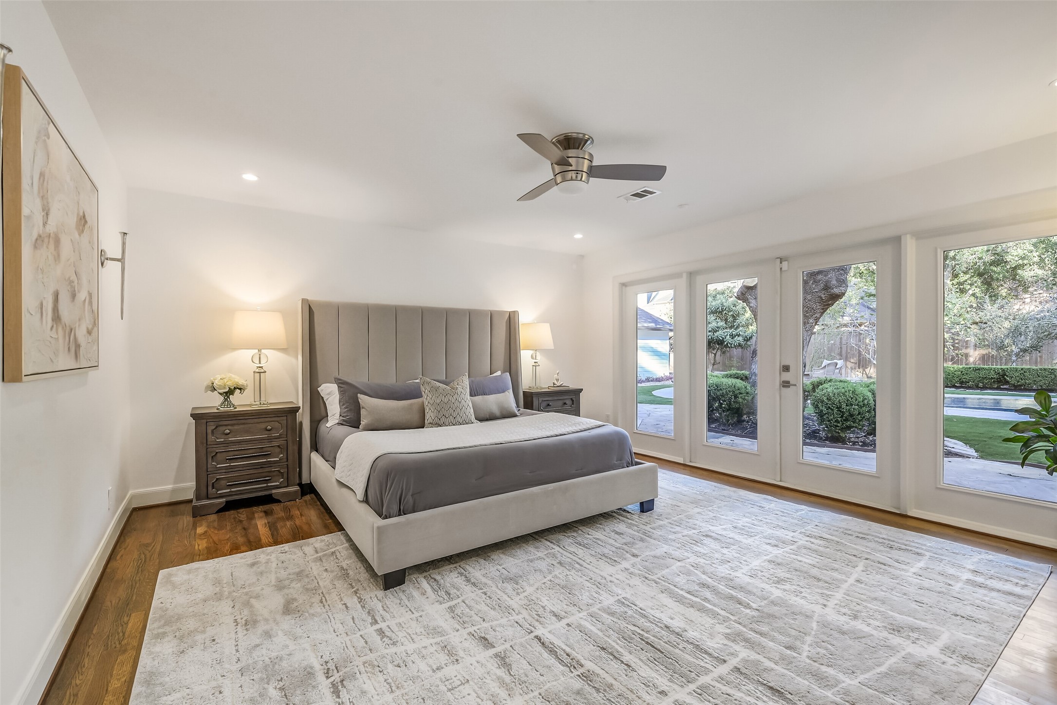 Spacious primary suite featuring rich hardwood floors, recessed lighting, and a wall of windows with French doors offering beautiful backyard views and direct patio access.