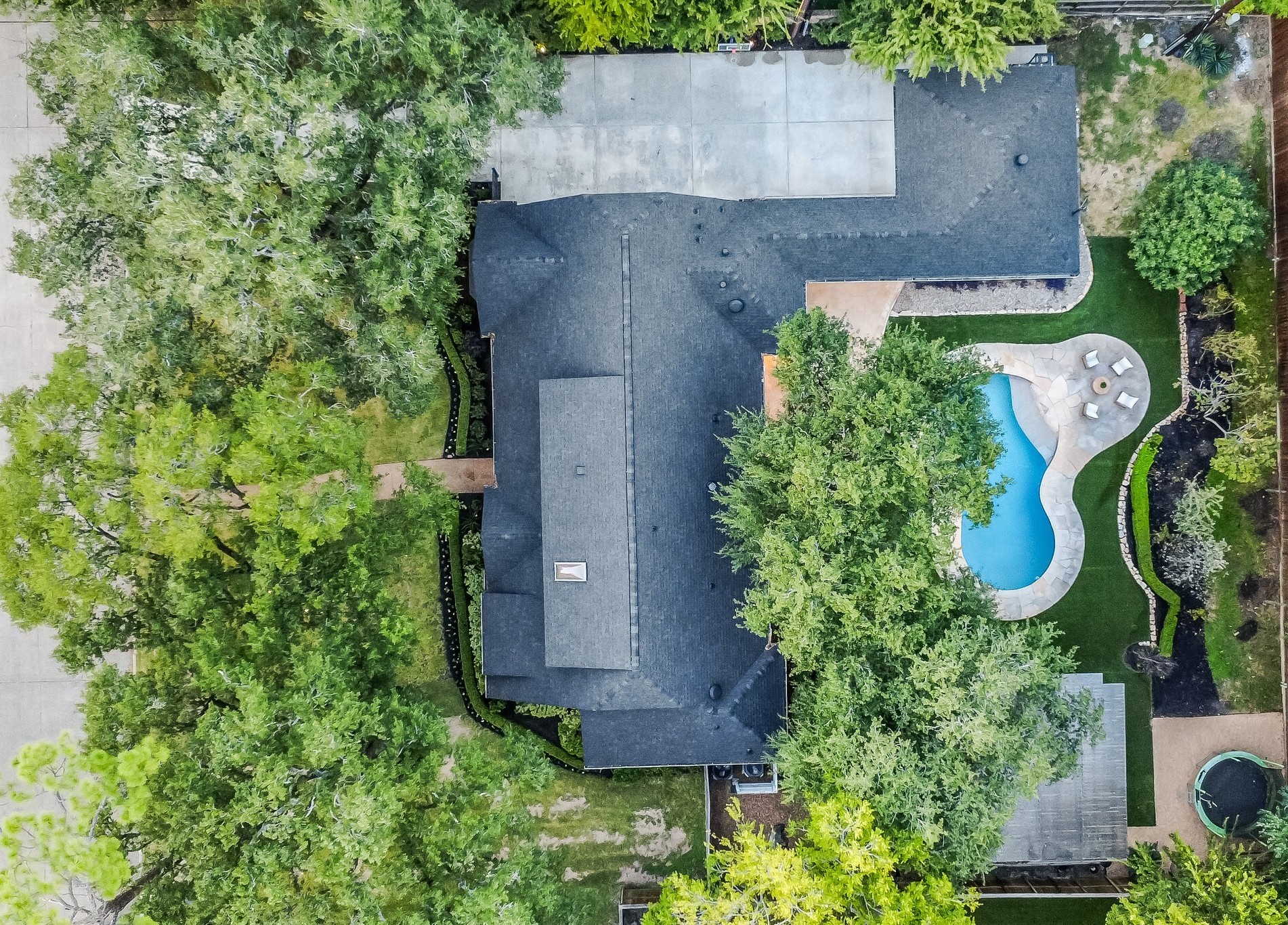 A unique aerial view capturing the home's expansive footprint, tree-shaded front yard, and beautifully designed backyard retreat.