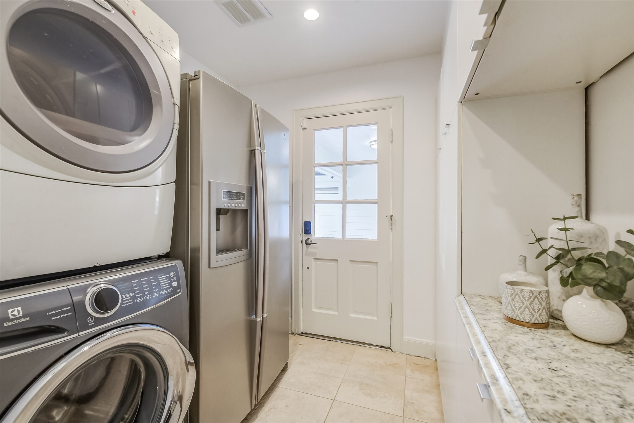 Convenient utility room featuring a stacked washer and dryer, additional refrigerator, built-in cabinetry for additional storage space, and direct access to the exterior.