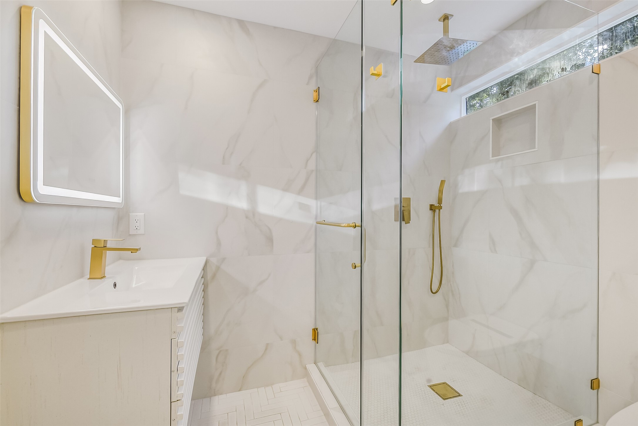 Contemporary secondary bathroom en-suite featuring a glass-enclosed shower with rainfall shower head, sleek gold fixtures, and a modern vanity with illuminated mirror.