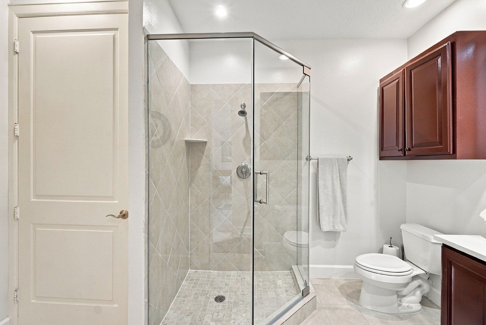 Well-appointed bathroom featuring a glass-enclosed shower, neutral tile, and generous vanity storage.